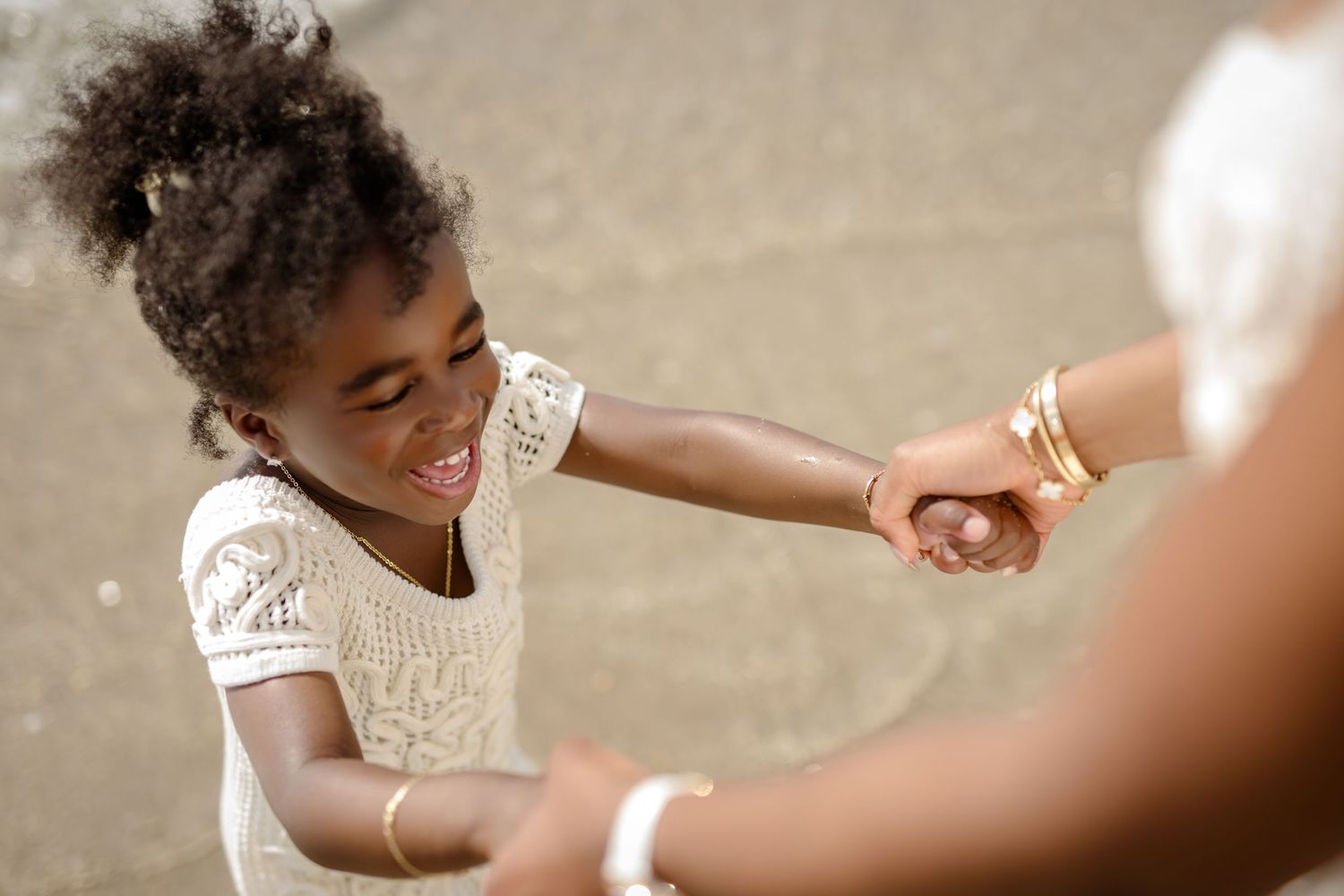 A close-up shot of hands touching on the beach while wearing white lace outfits.