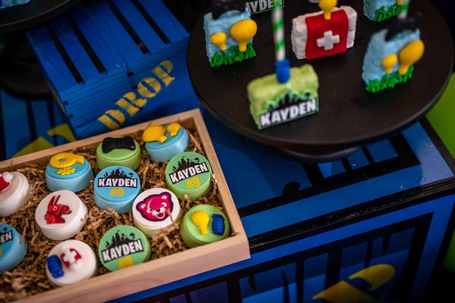 Colorful cupcakes decorated with video game themed designs displayed in a wooden box and on a dark platform.