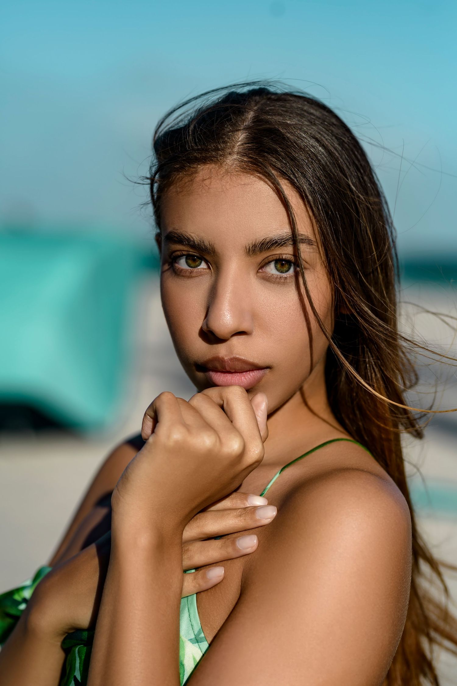 Portrait of a woman with windswept hair posing on a beach with turquoise water in the background.
