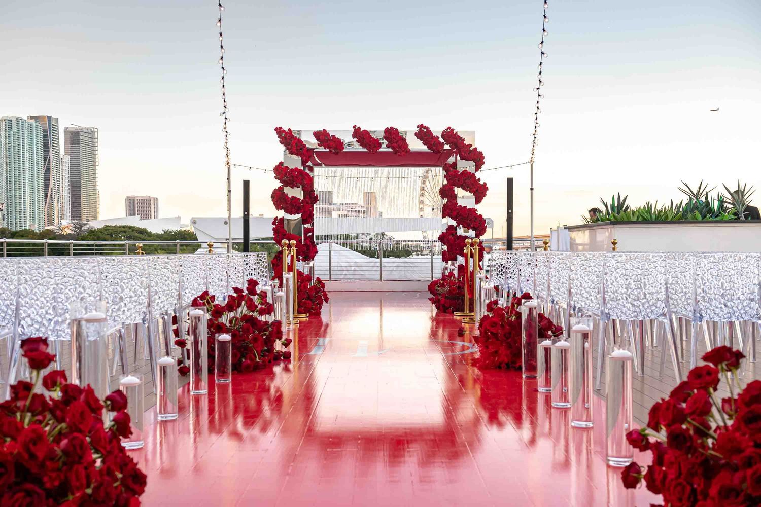 Elegant wedding ceremony setup with red flower arch and white chairs overlooking city skyline on the Seafair Mega Yacht in Miami.