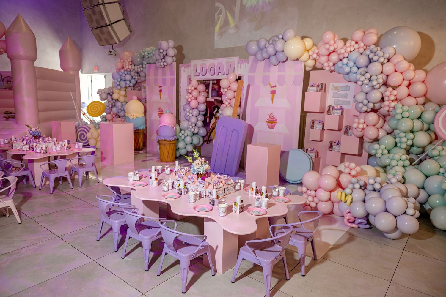 Pastel pink and blue balloon garlands decorate a luxurious event space with elegant table settings and floral arrangements.