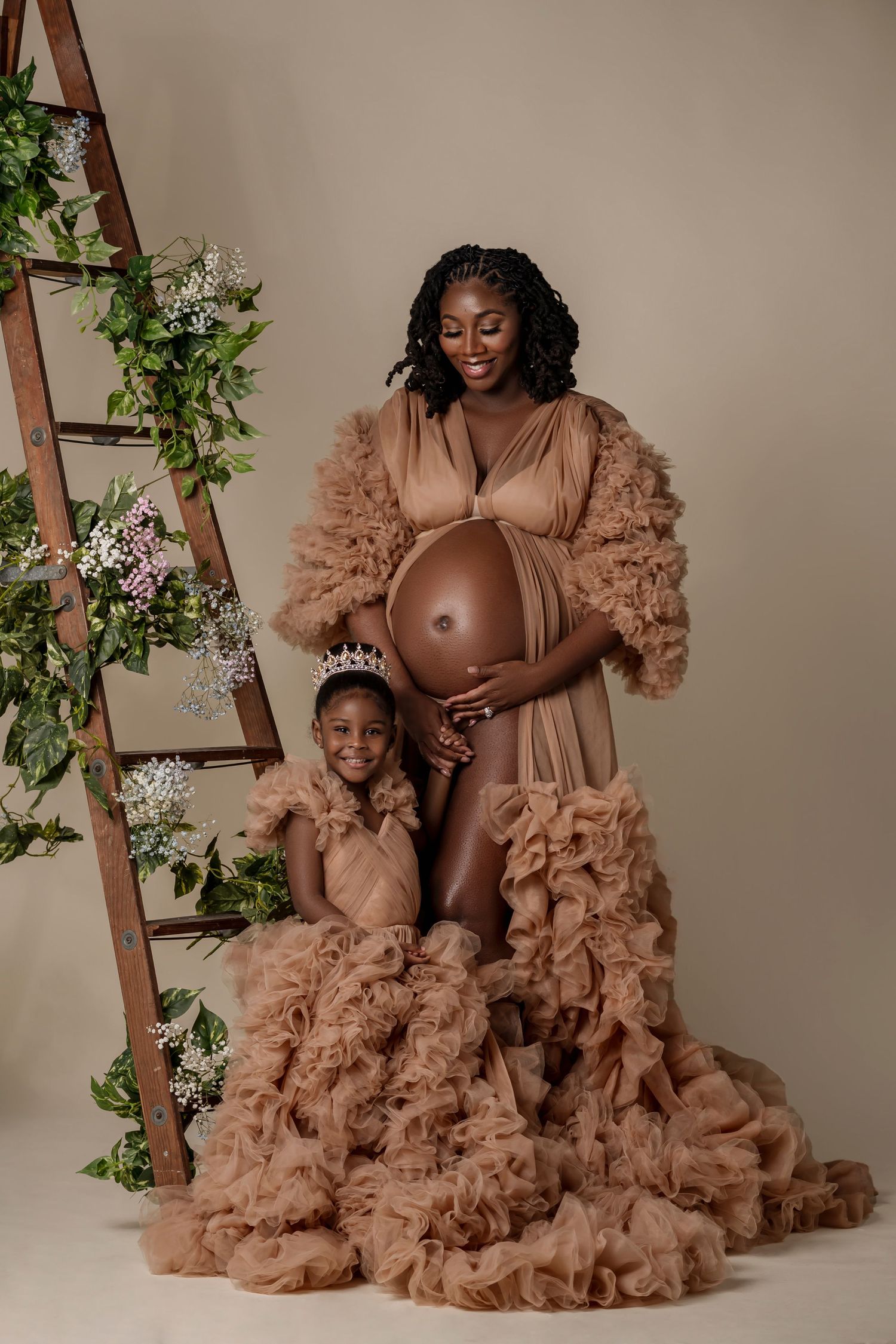 Dreamy maternity photoshoot featuring brown ruffled dresses against a neutral backdrop with decorative ivy and ladder.
