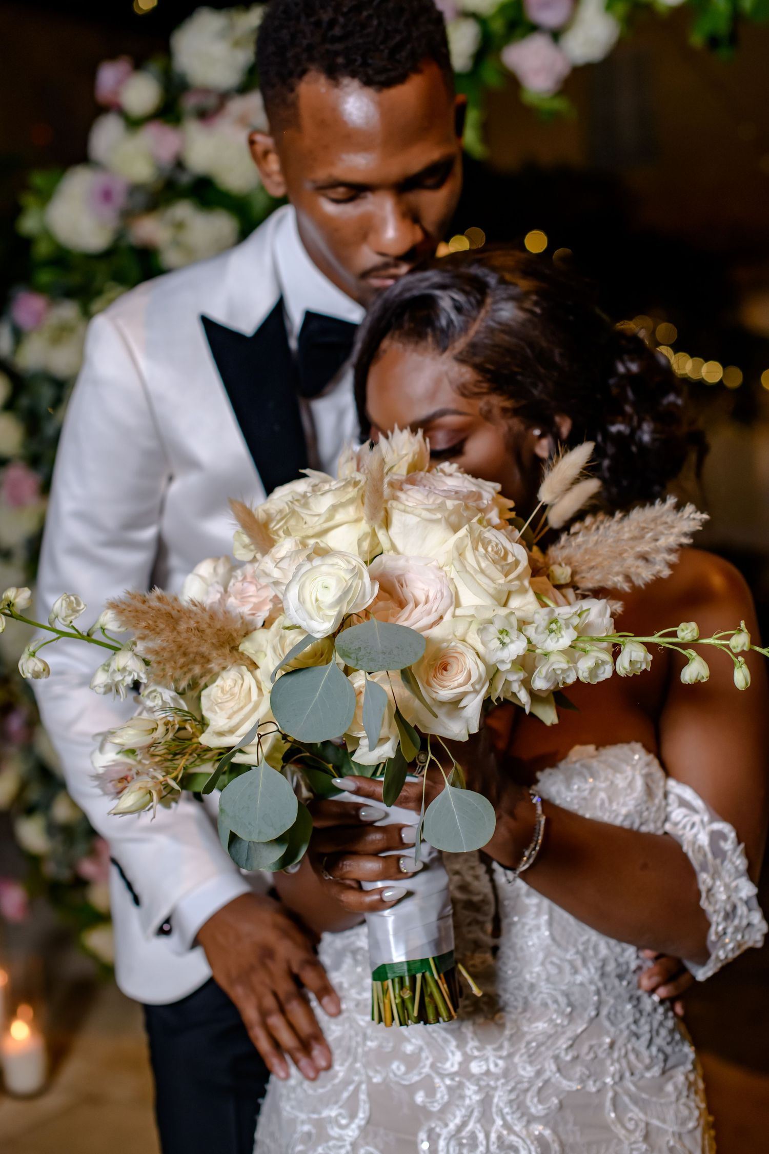 Wedding couple sharing intimate moment with elegant white and blush floral bouquet.