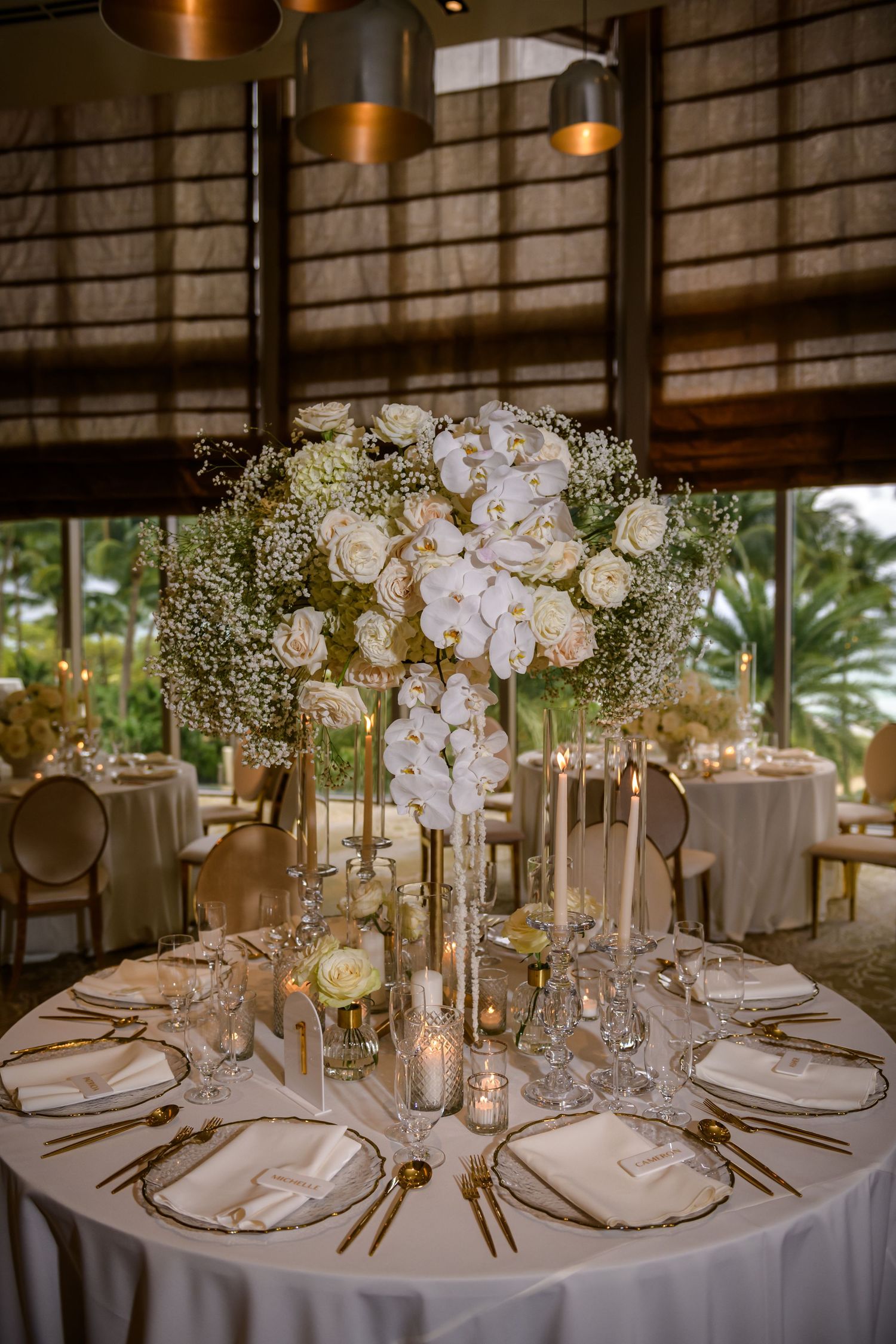 Luxurious wedding reception venue with multiple round tables decorated with white floral centerpieces and ambient lighting.