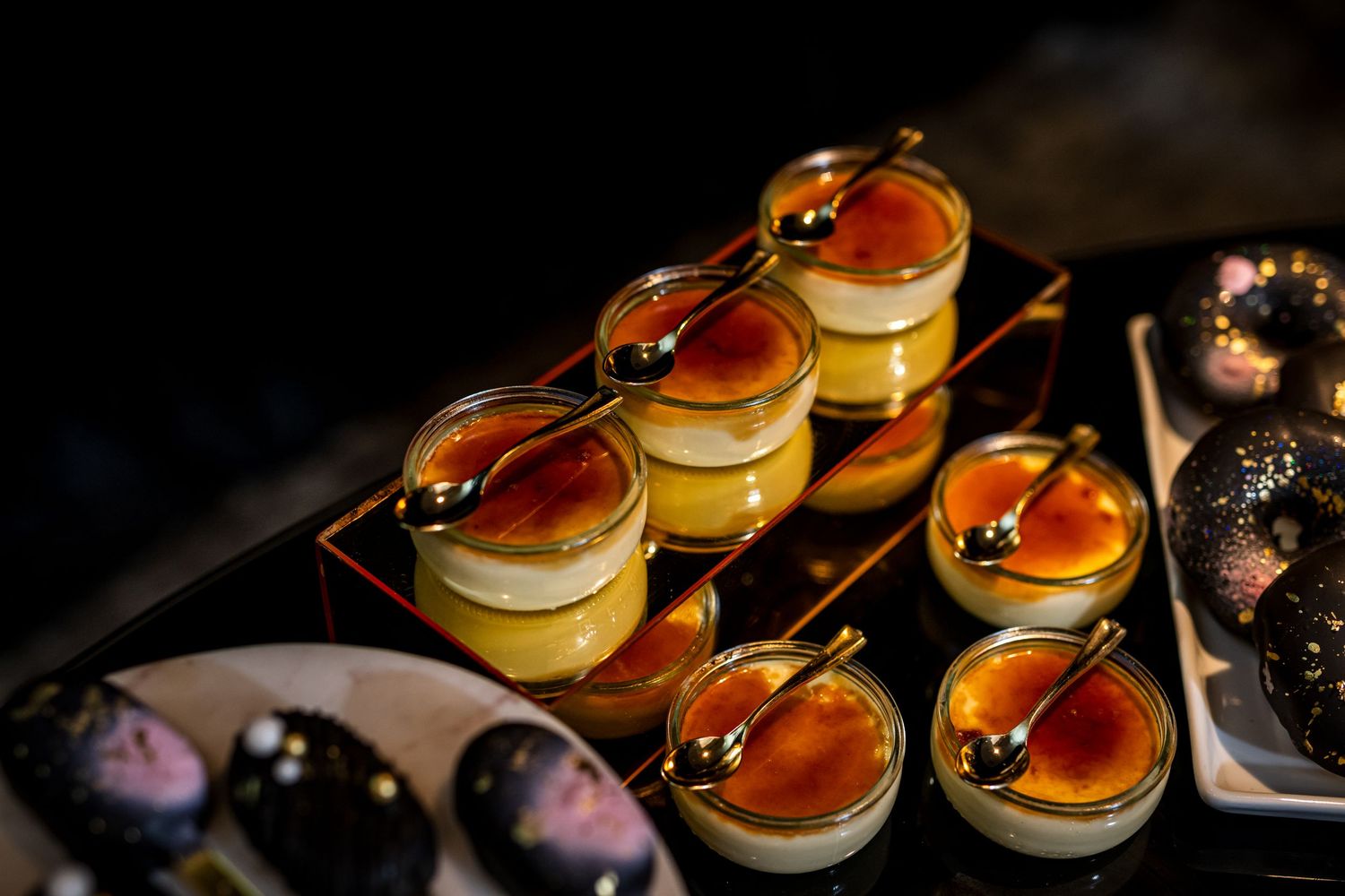 Elegant dessert cups filled with yellow custard and topped with caramel sauce arranged on dark serving trays.