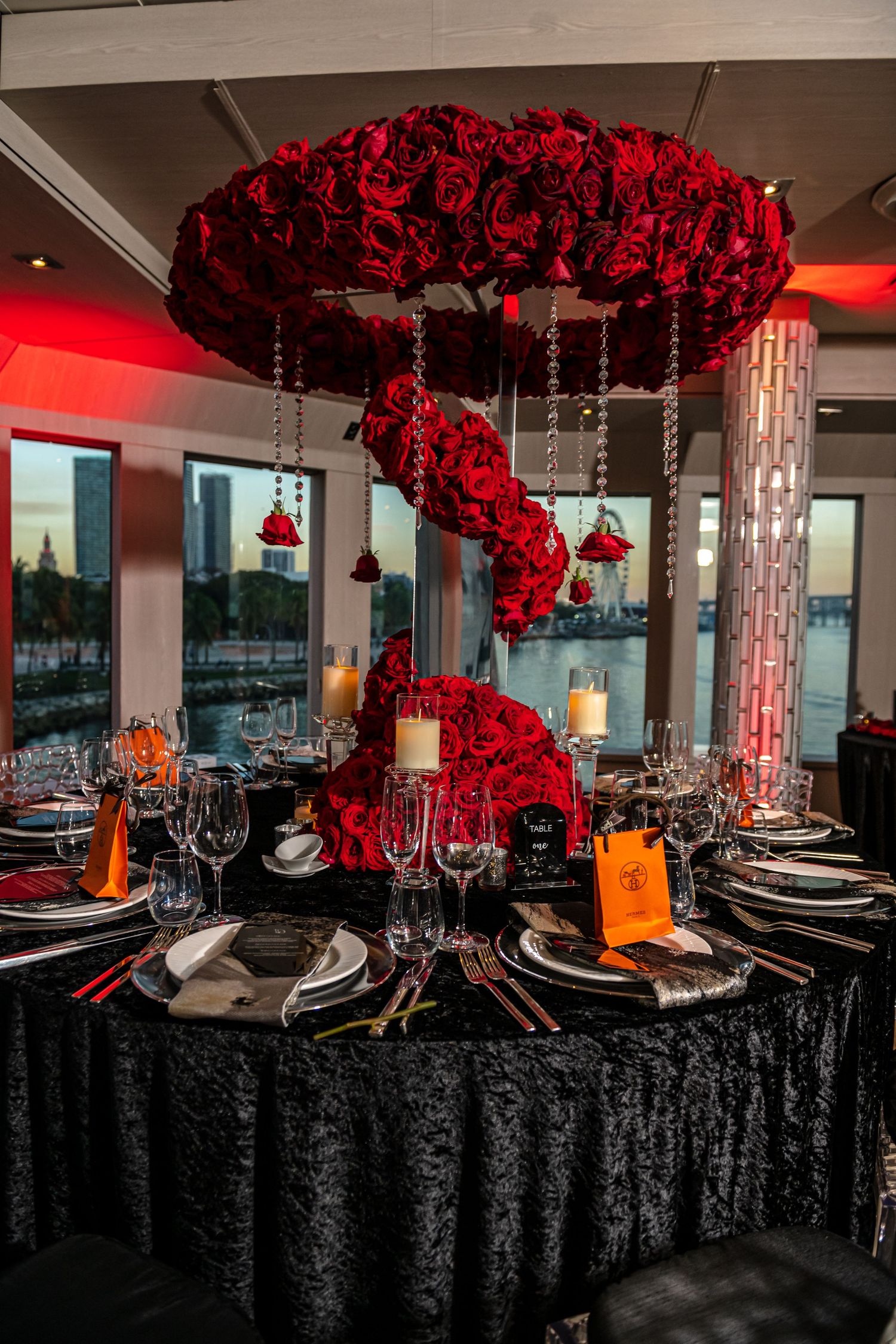Elegant dining tables with black tablecloths and dramatic red rose centerpieces create a luxurious event space setting.