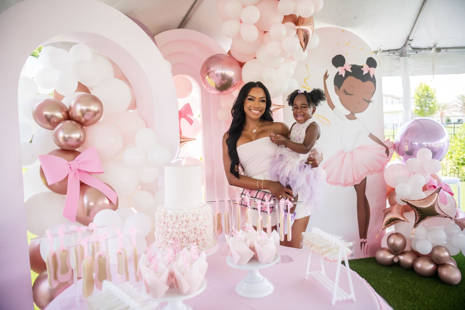 Pink and white balloon arch decorates a baby celebration event with dessert table.
