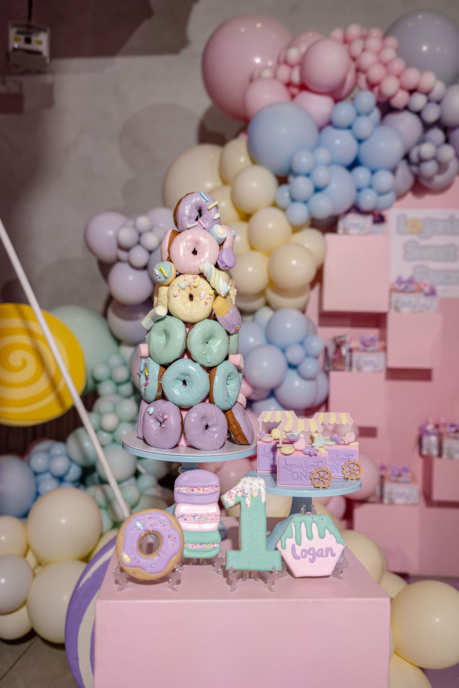 Pastel balloon garland decorates a dessert table with macarons and sweets in soft pink, blue and purple tones.