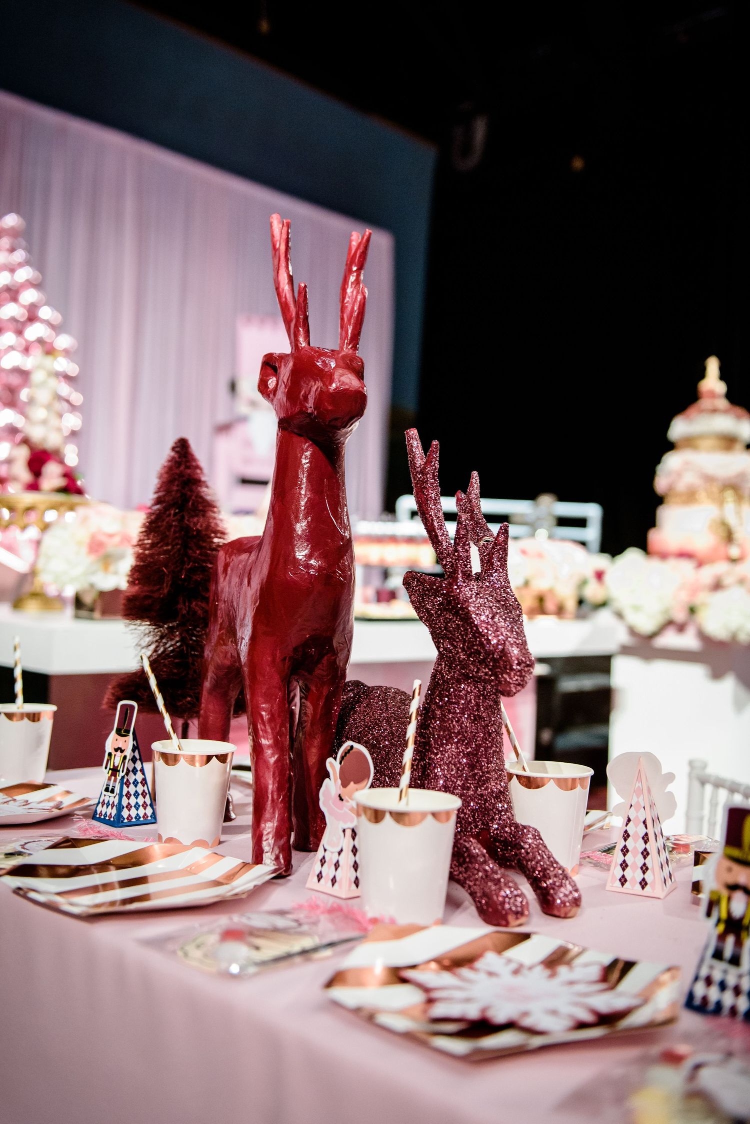 Festive holiday table setting with red and pink glittery reindeer decorations and Christmas trees in the background.