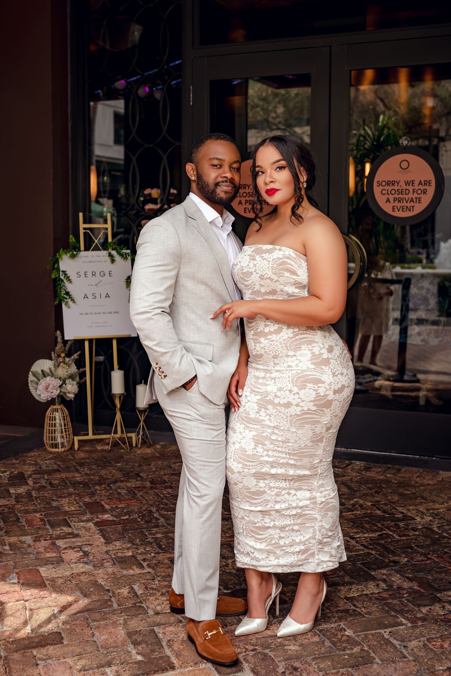 Elegant couple posing in coordinating beige outfits outside a venue closed for a private event.