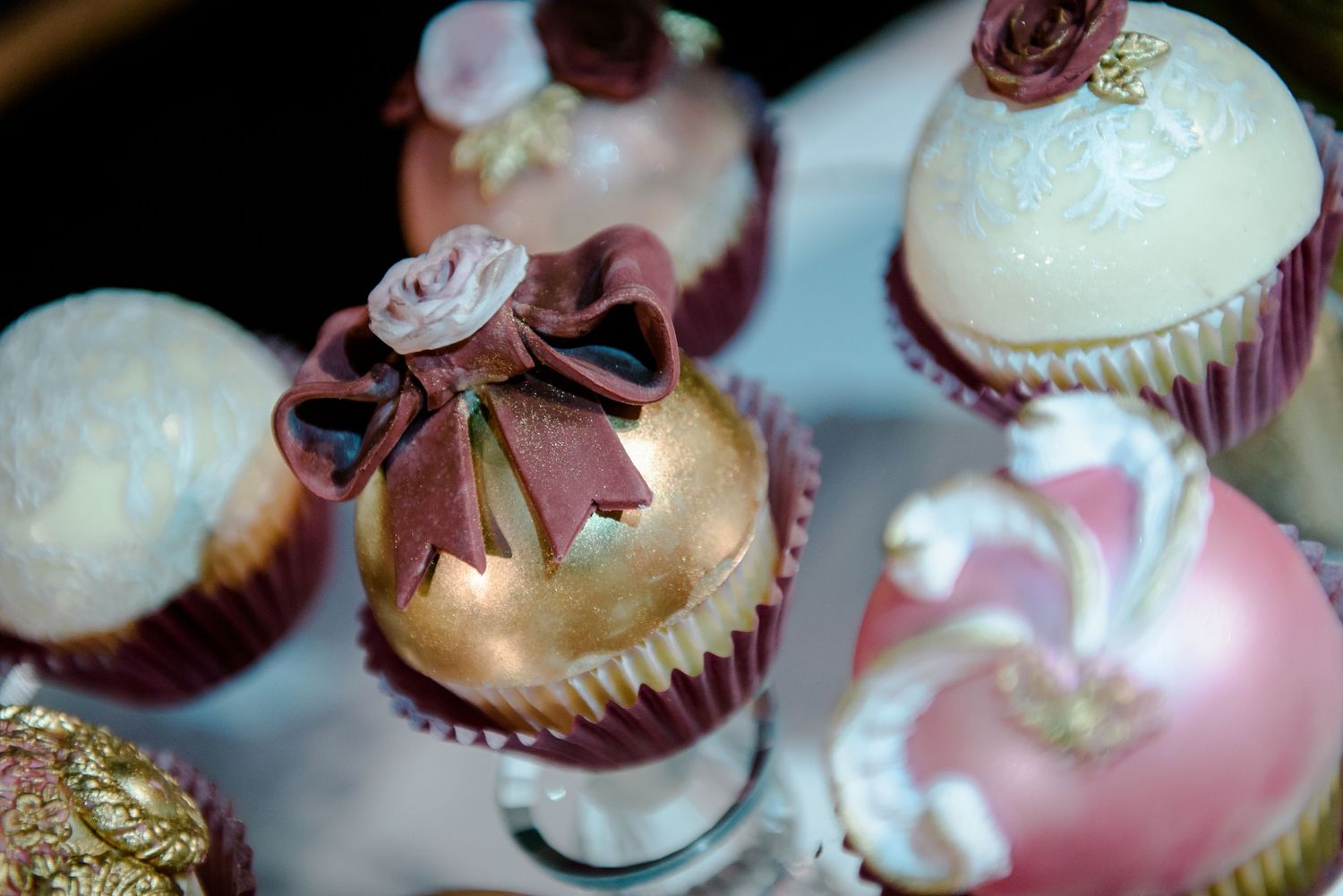 Elegant pink and white frosted cupcakes decorated with delicate roses and gold accents arranged in a display.