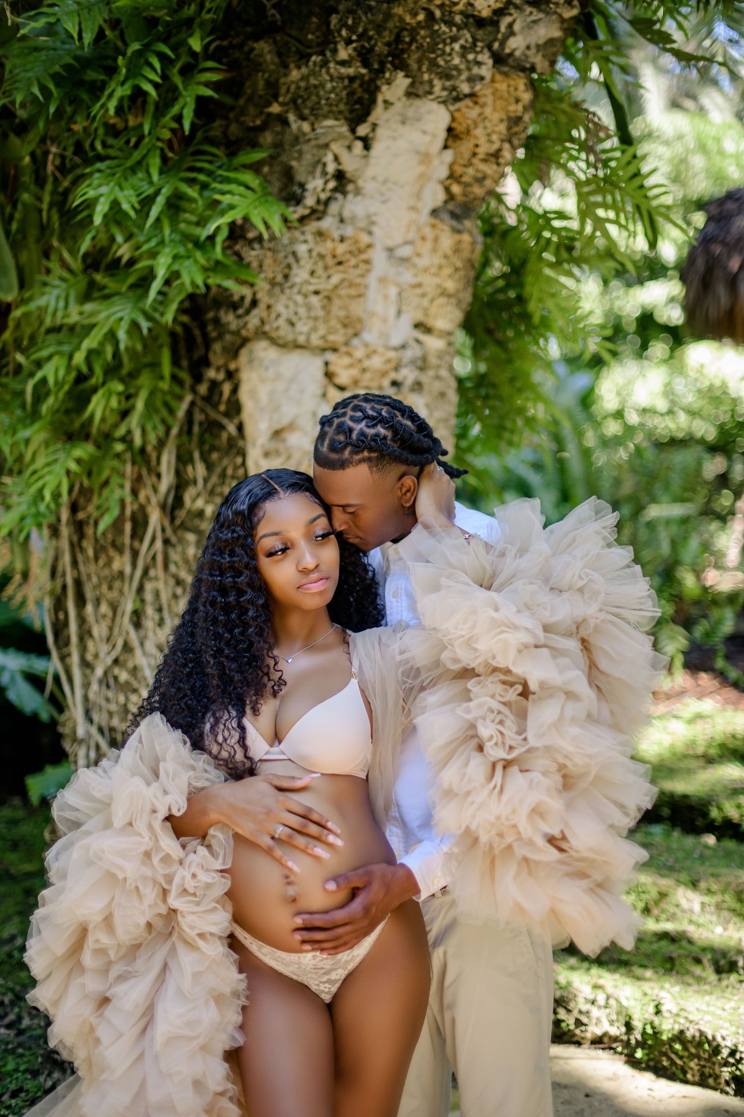 A romantic maternity photoshoot in a garden setting with flowing tulle fabric.