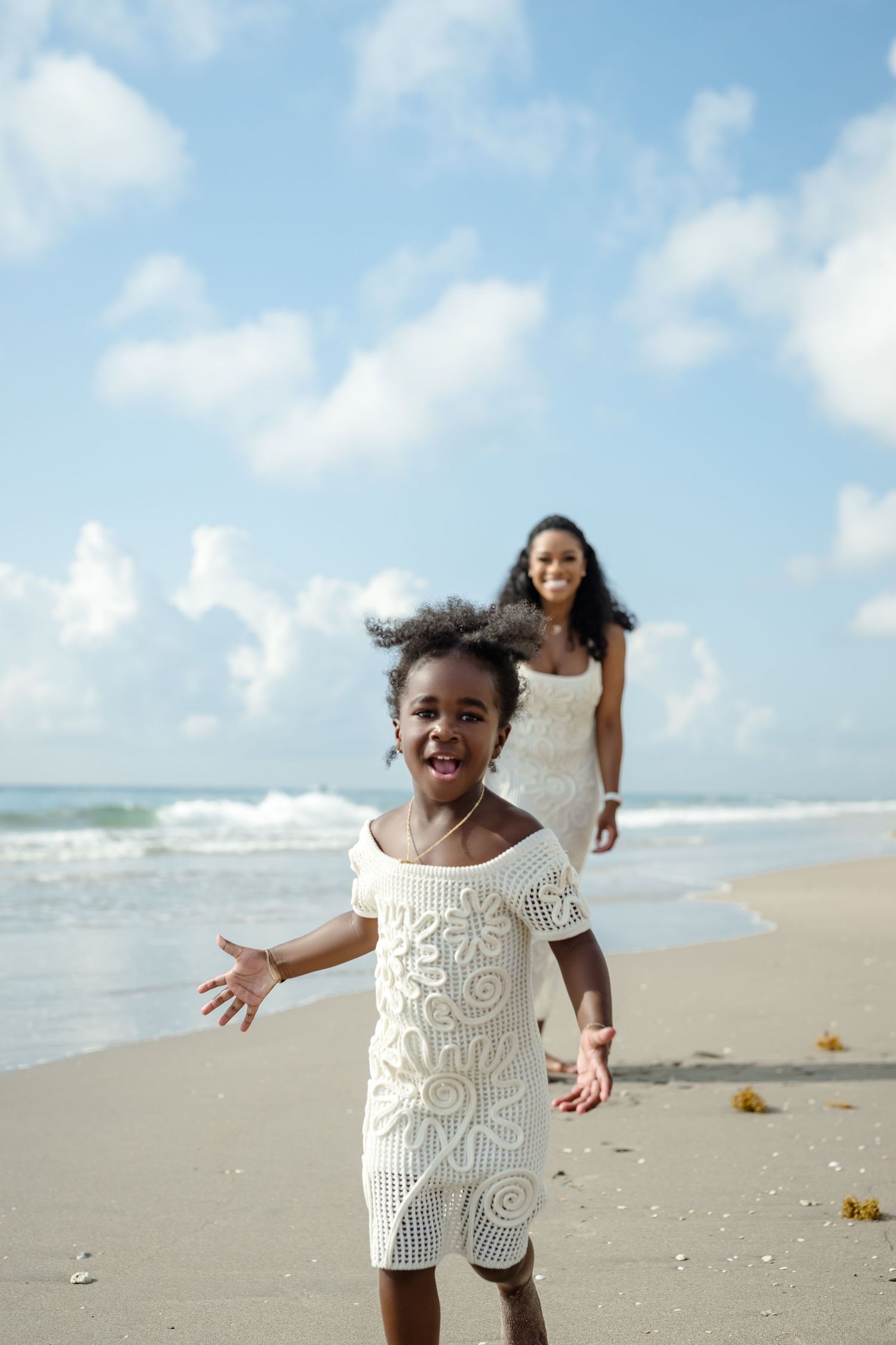 Two people in white lace dresses enjoying a carefree moment on a sunny beach.