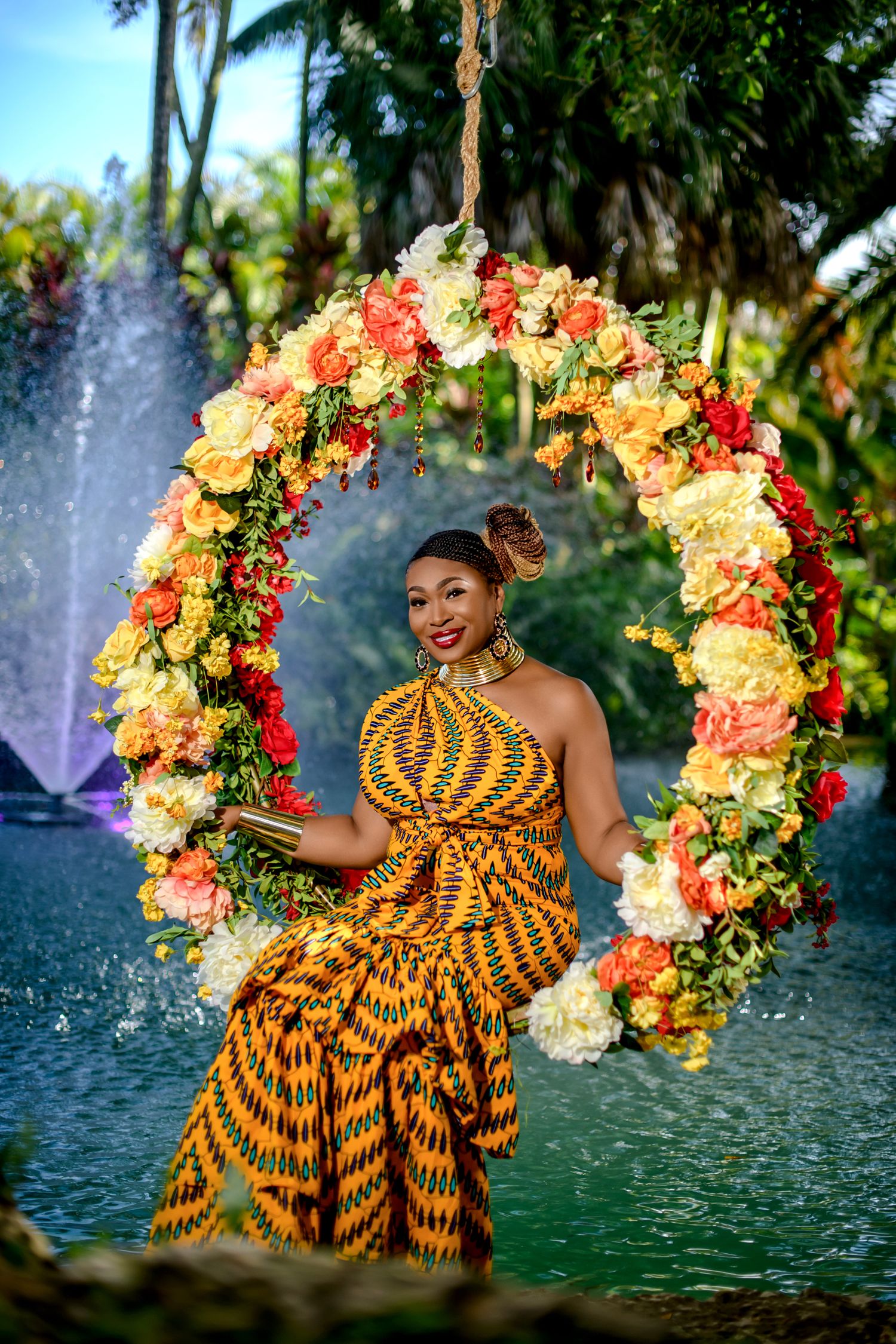A floral wreath frames a figure in a vibrant yellow and black patterned dress against a fountain backdrop.