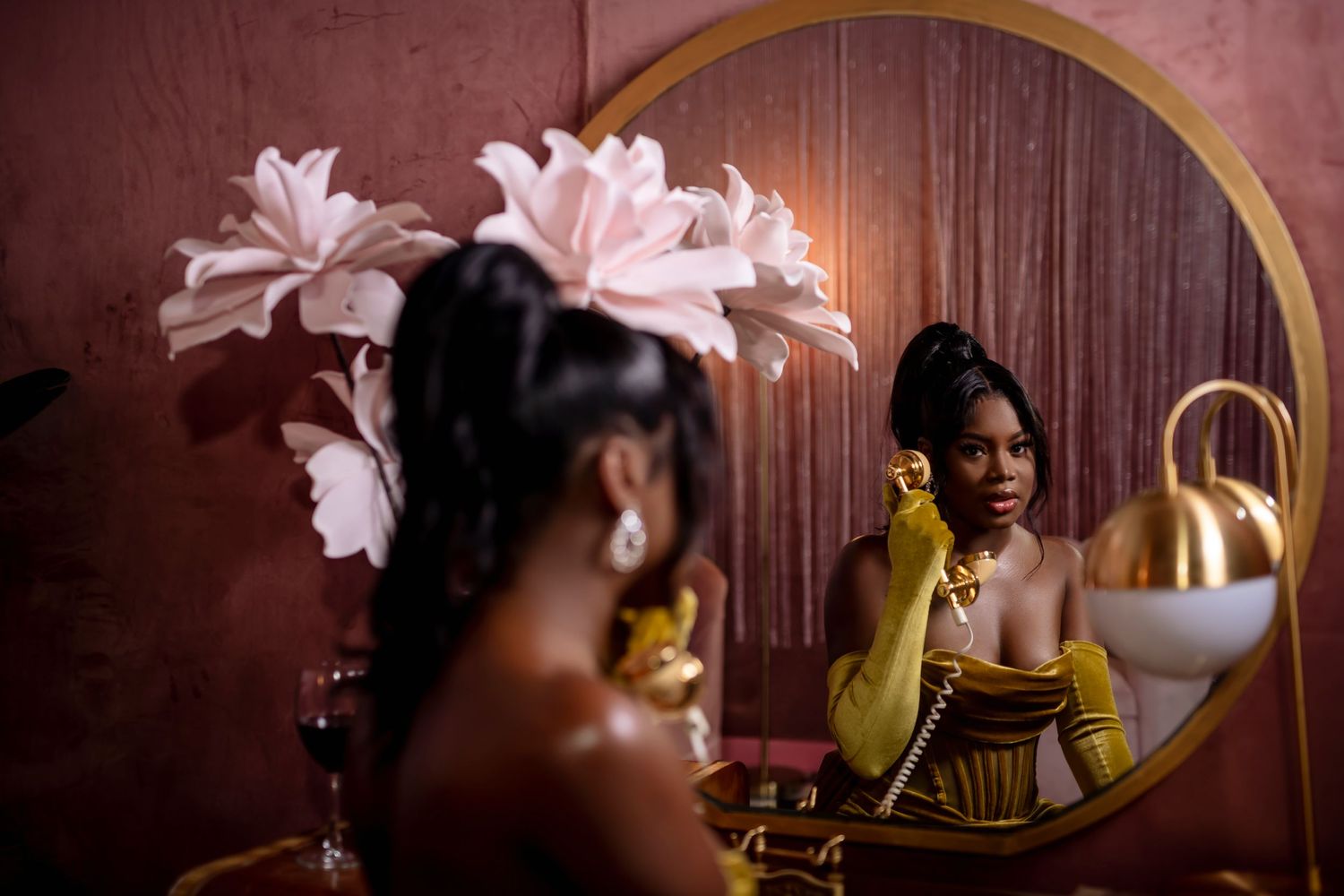 Person in yellow top looking at reflection in decorative mirror with pink flowers.