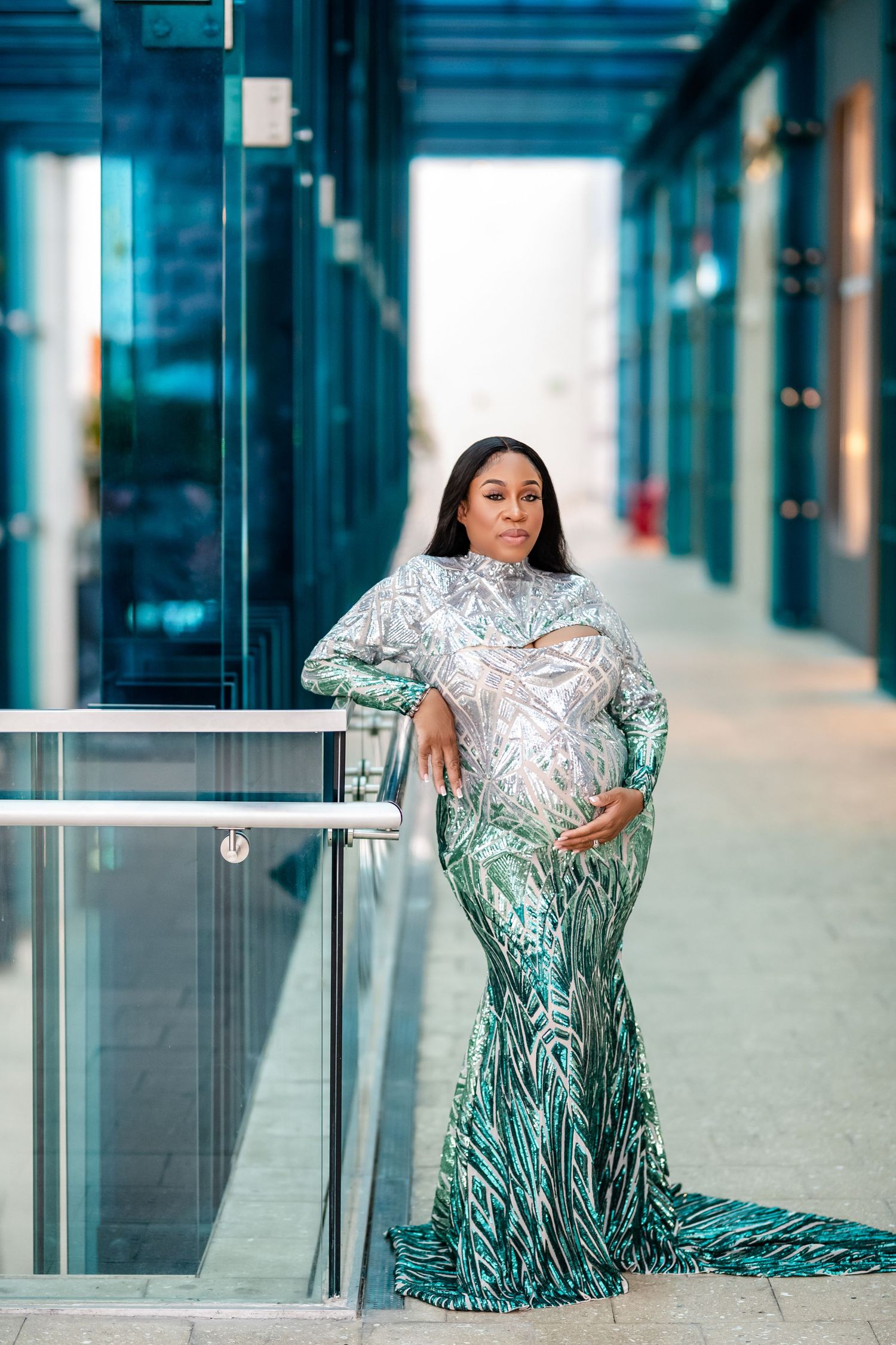 Elegant evening gown in silver and teal ombre with sequined pattern and mermaid silhouette in modern hallway setting.