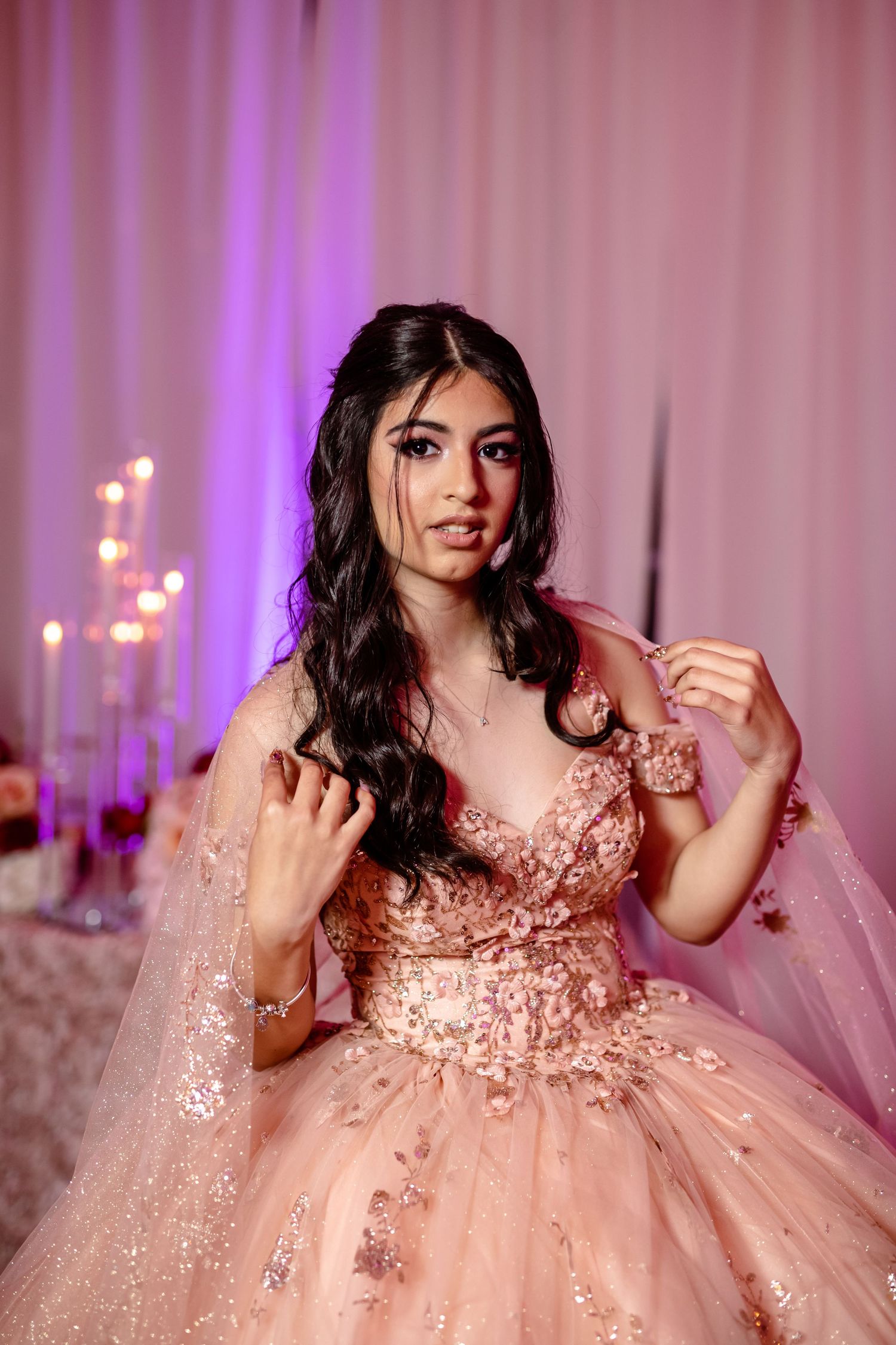 A sparkly pink quinceañera dress with intricate beading and tulle details in a purple-lit venue.