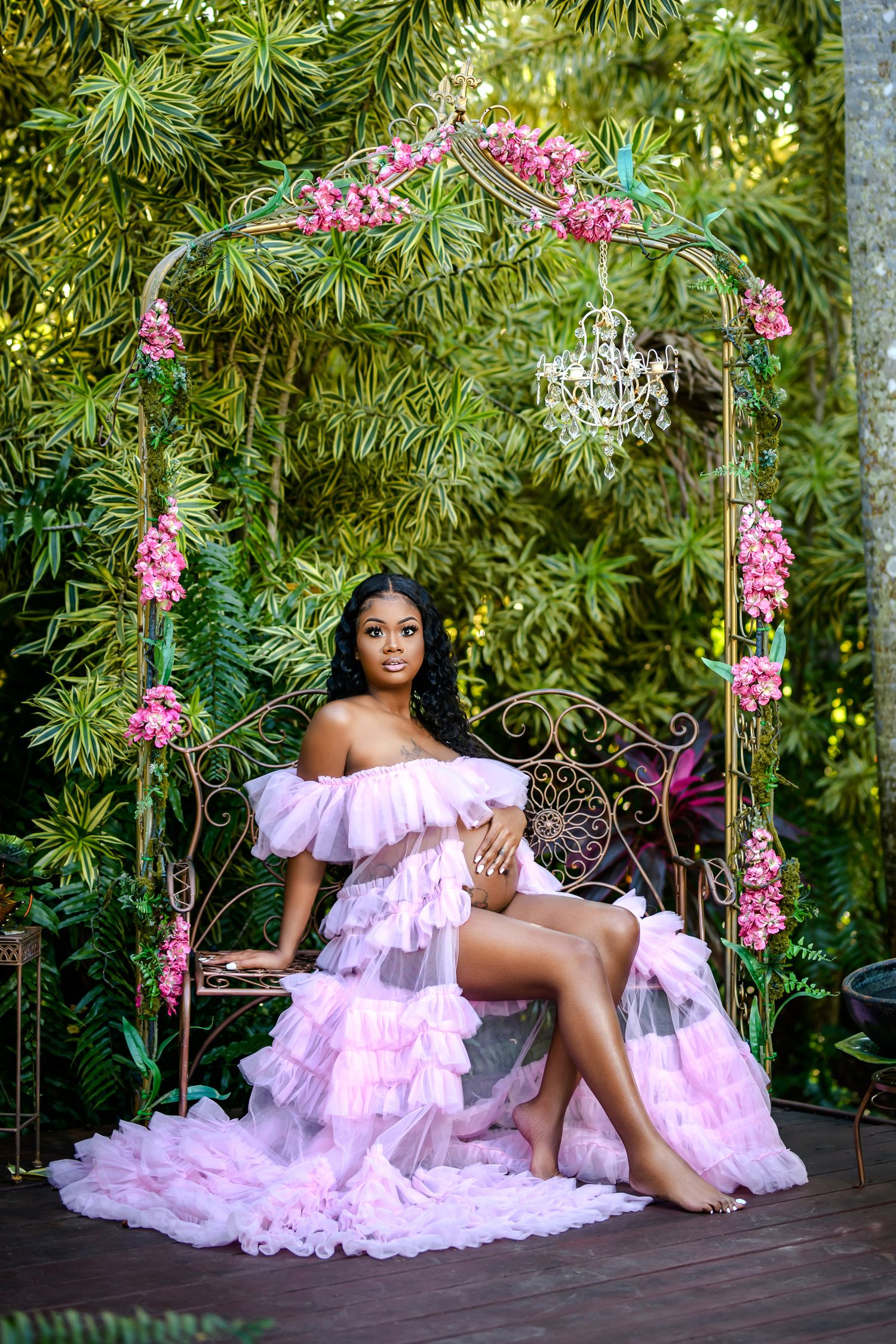 A pink tulle gown flows gracefully across an outdoor garden setting with tropical foliage and hanging orchids.