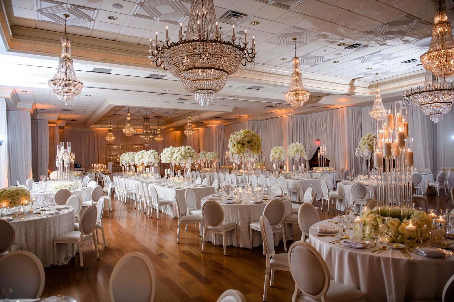 Luxurious ballroom wedding reception with crystal chandeliers and elegant white table settings.