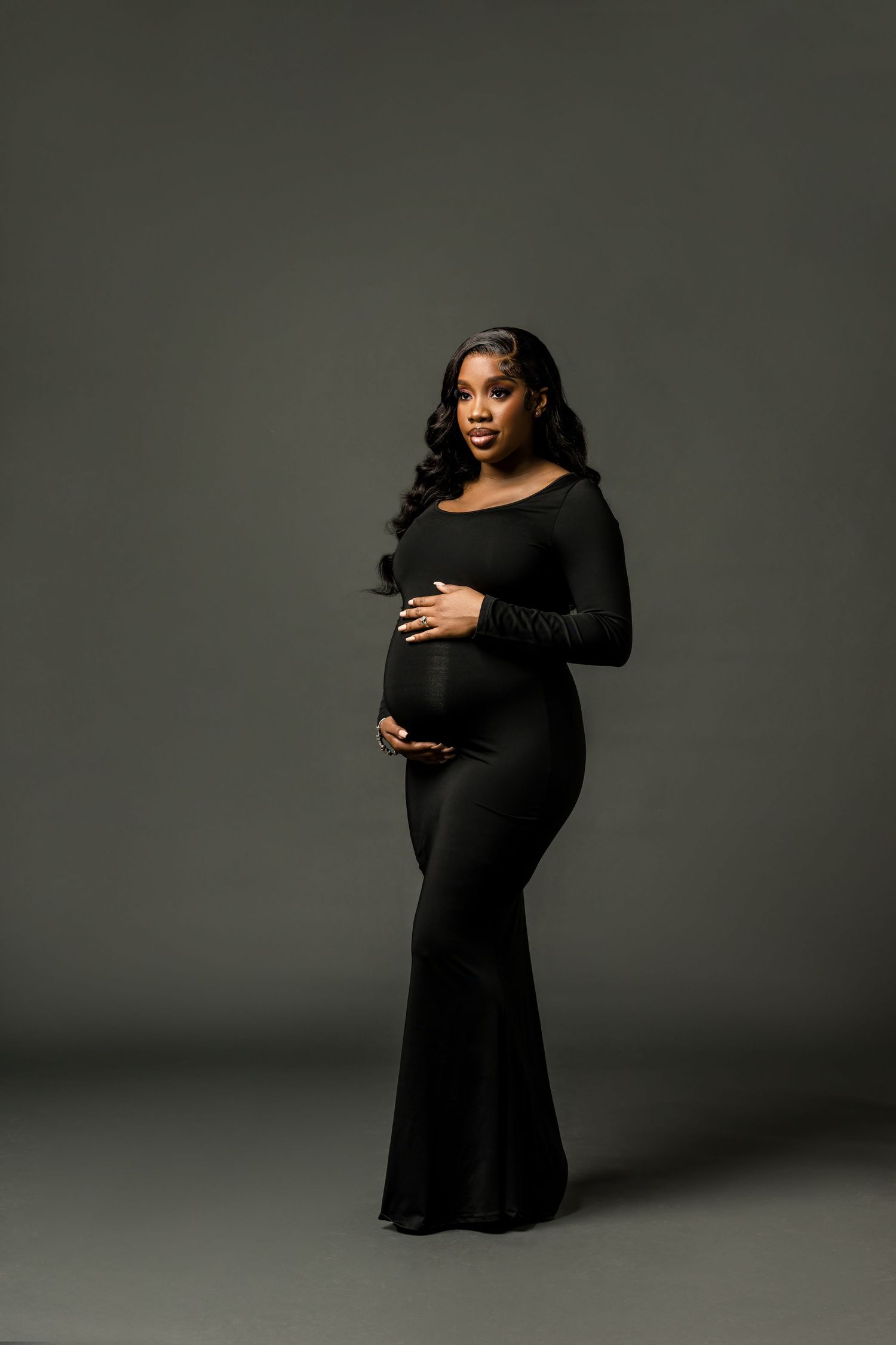 A series of maternity photos showing a woman in a black dress posing against a dark grey backdrop.