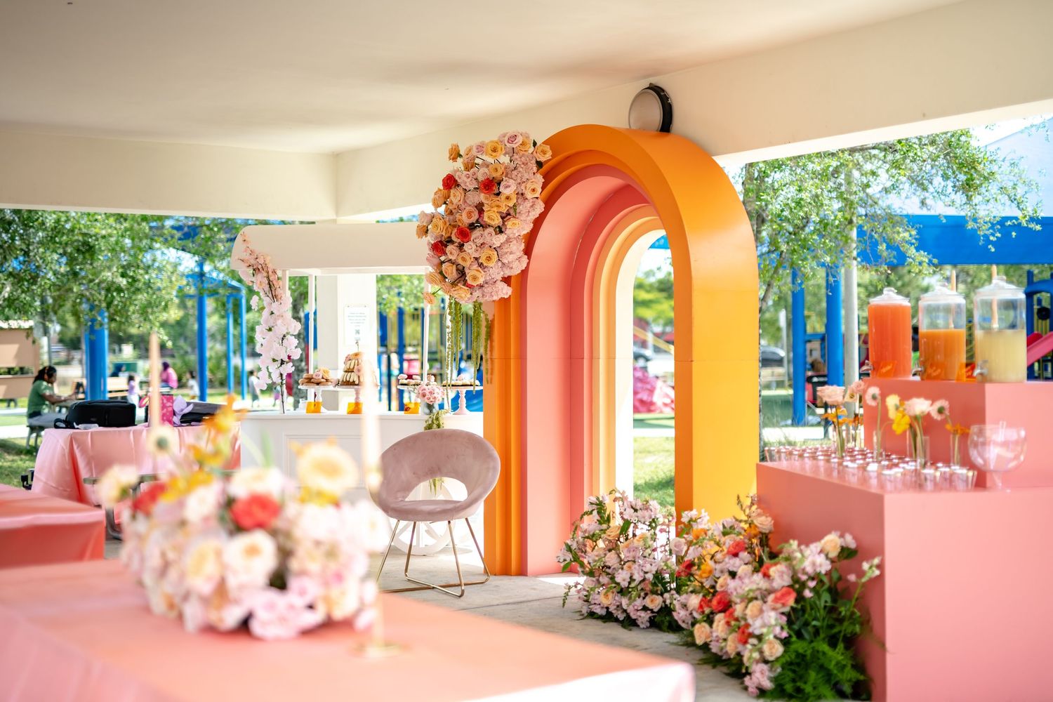 A colorful indoor-outdoor event space features pink and orange archways with floral decorations and modern furniture.