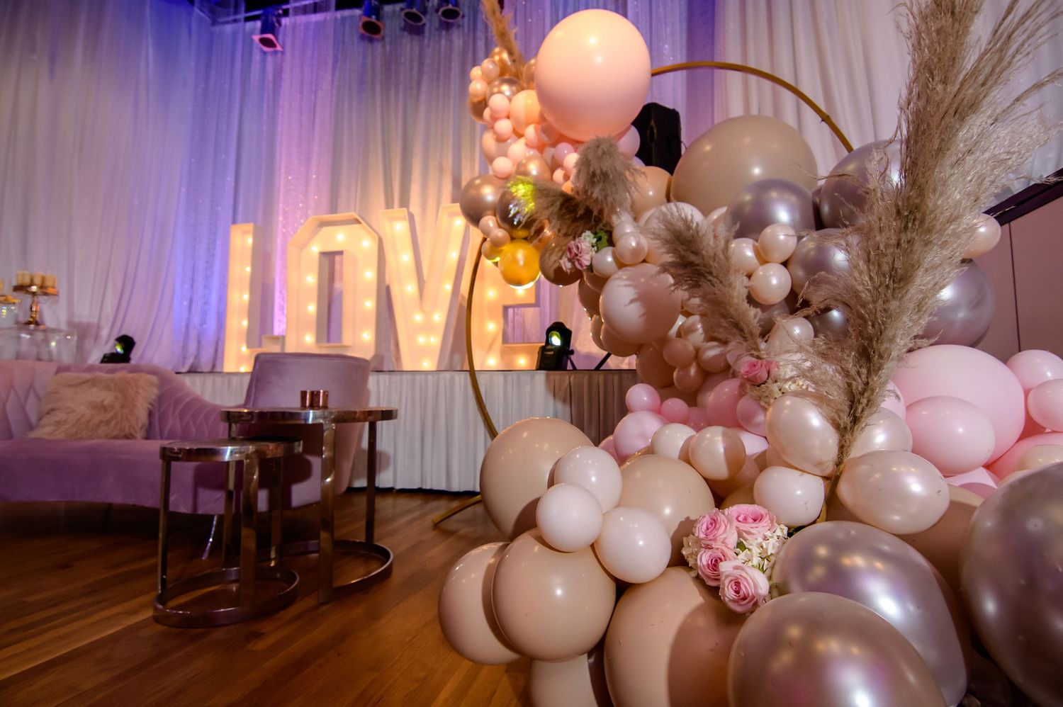 Elegant event space decorated with white drapes, pink balloons, and pampas grass creating a romantic atmosphere.