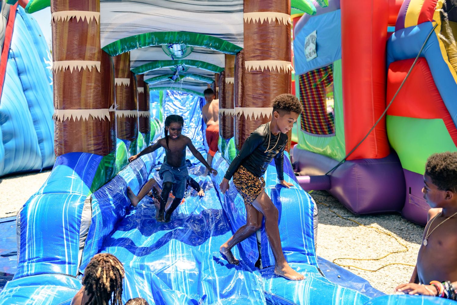 A blue inflatable water slide with palm tree decorations stands ready for summer fun at an outdoor event.