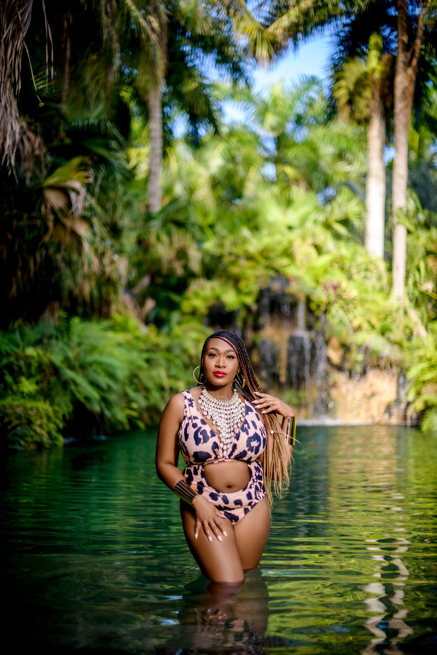 Woman in leopard print swimsuit poses in tropical lagoon surrounded by lush palm trees and greenery.