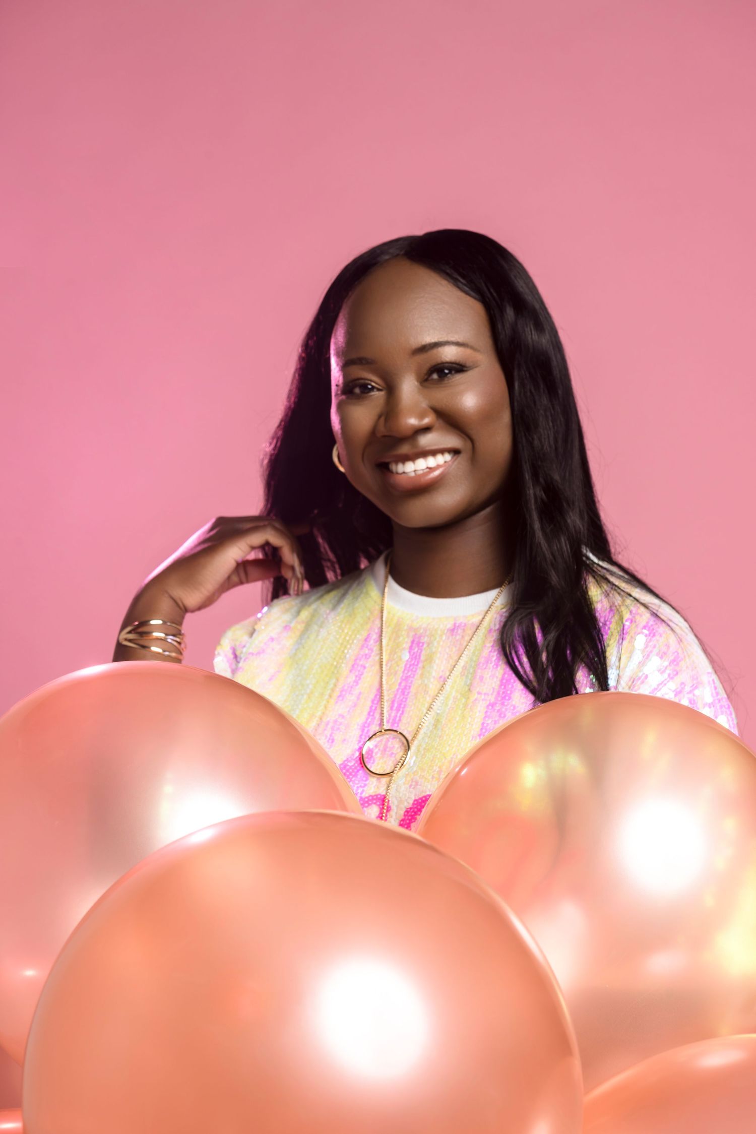 Person in pink outfit smiling and posing with large pink balloons against a pink background.