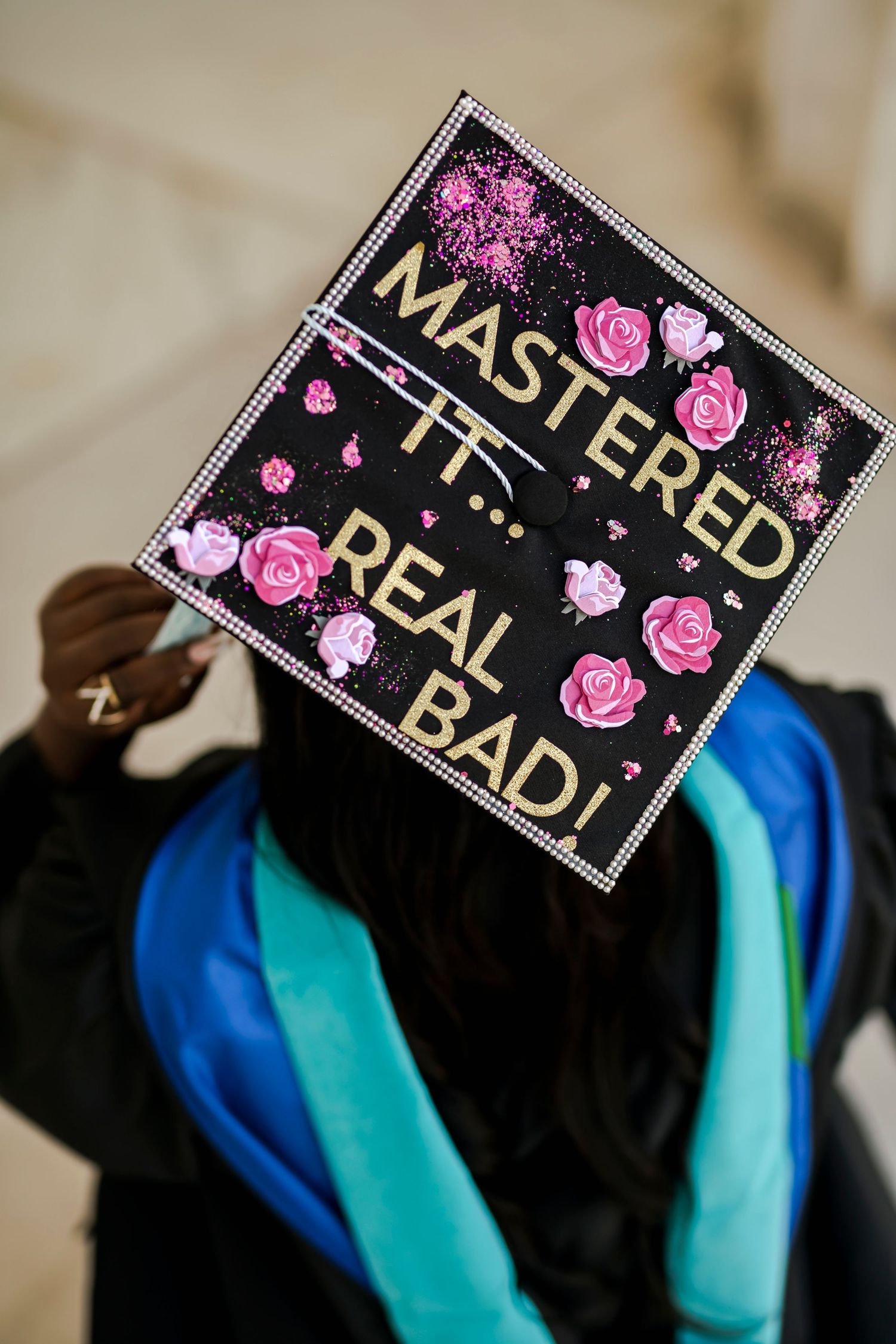 A series of graduation caps decorated with pink roses and gold text against a black background.