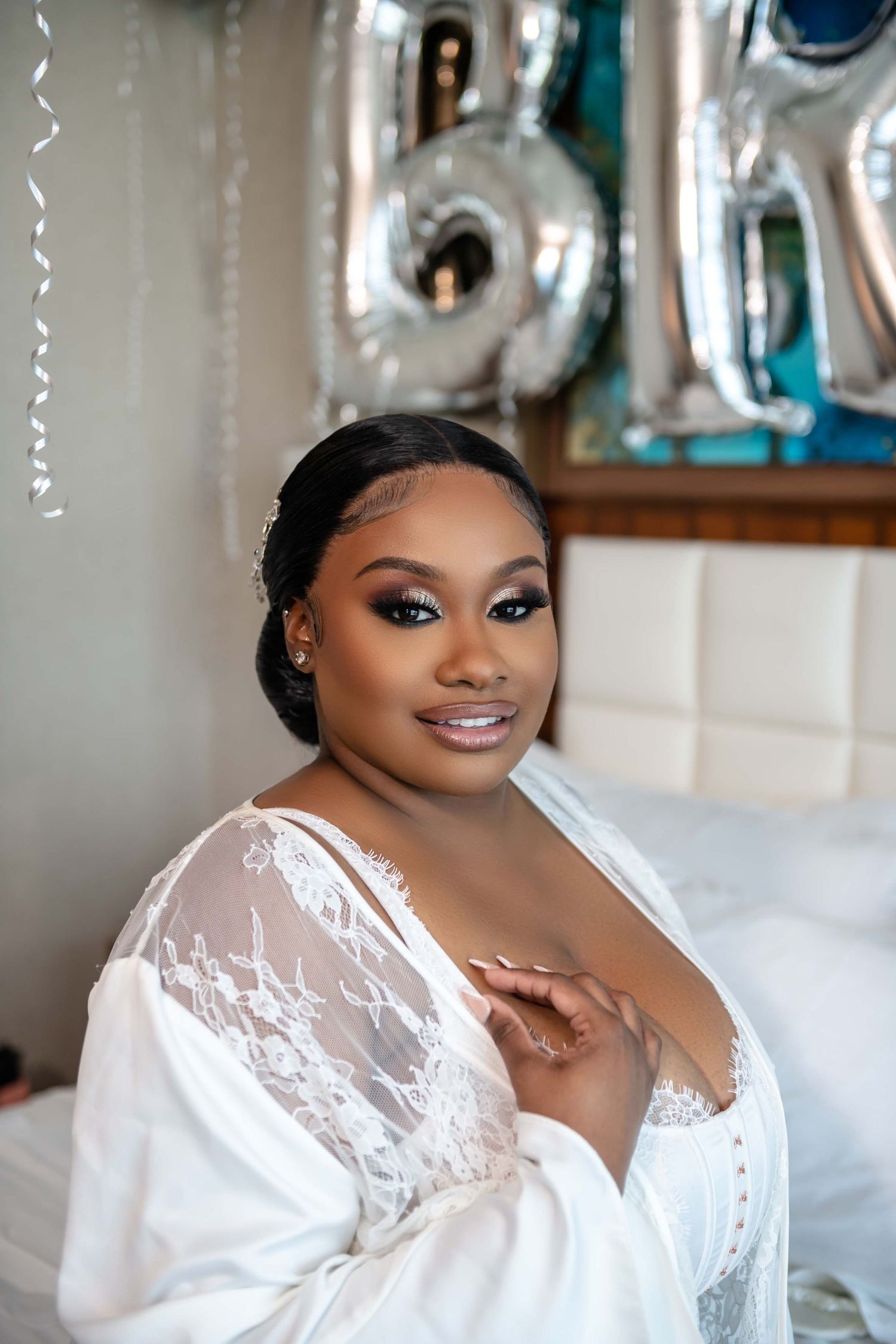 Bridal portrait with silvery balloons showing elegant makeup and white lace robe.