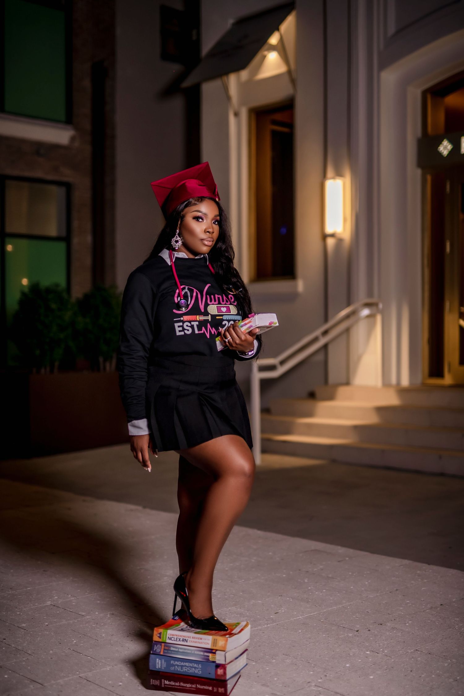 A person in a black hoodie and pink hat poses with a book in a dimly lit hallway at night.