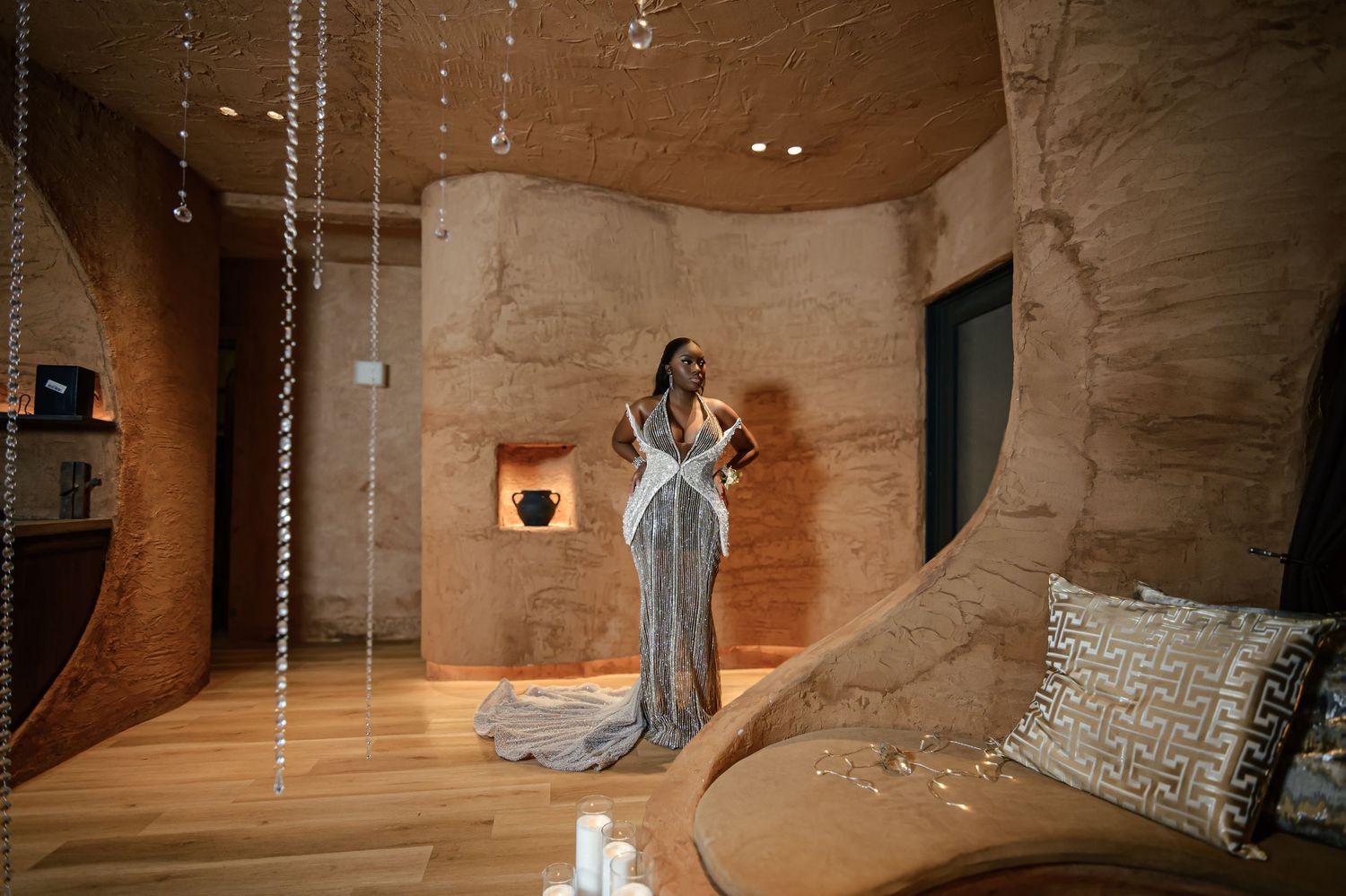 Woman in elegant silver gown poses in a luxury cave-like interior with warm stone walls and crystal decor.