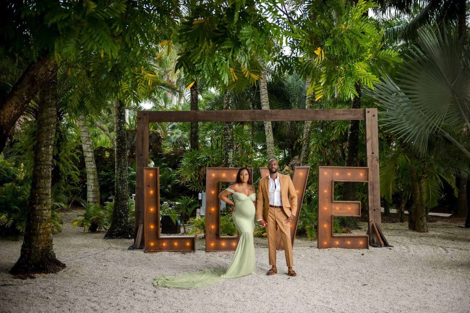 A scenic wooden pathway winds through a lush tropical garden with palm trees and greenery.