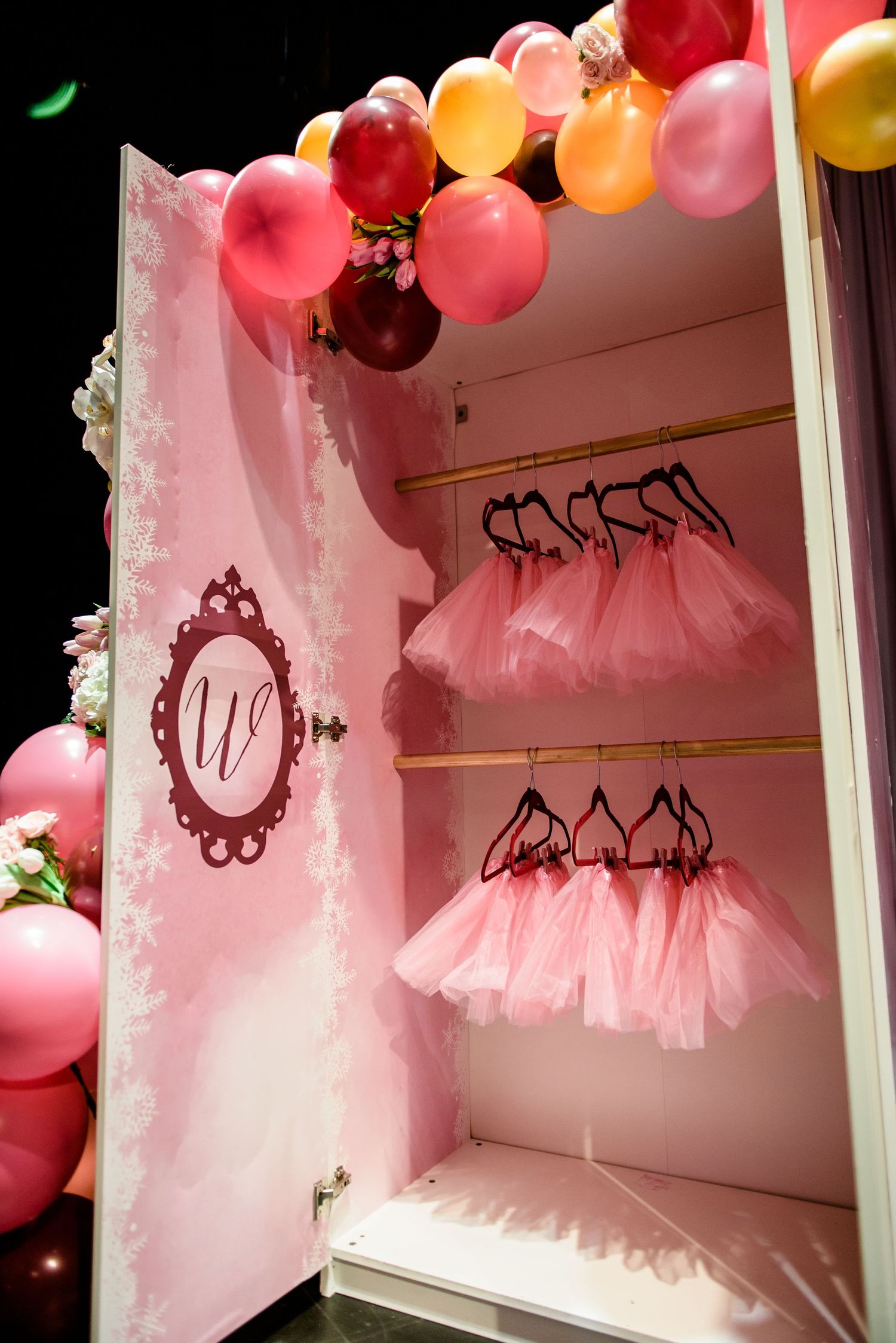 Pink tulle dresses hang in a boutique display with colorful balloons and ornate wall decorations creating a dreamy atmosphere.