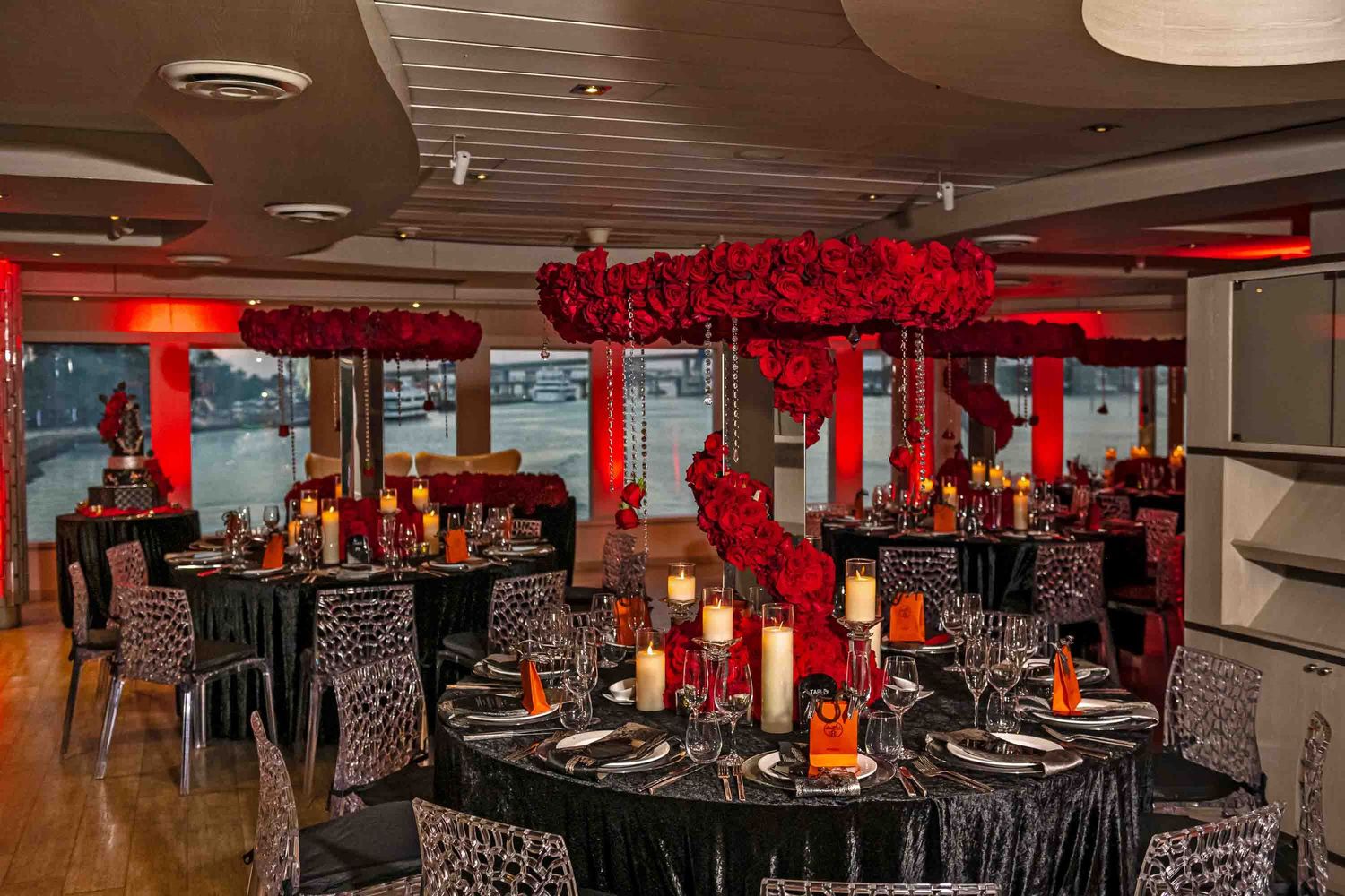 Elegant dining room setup with black tablecloths and dramatic red rose centerpieces under red ambient lighting.
