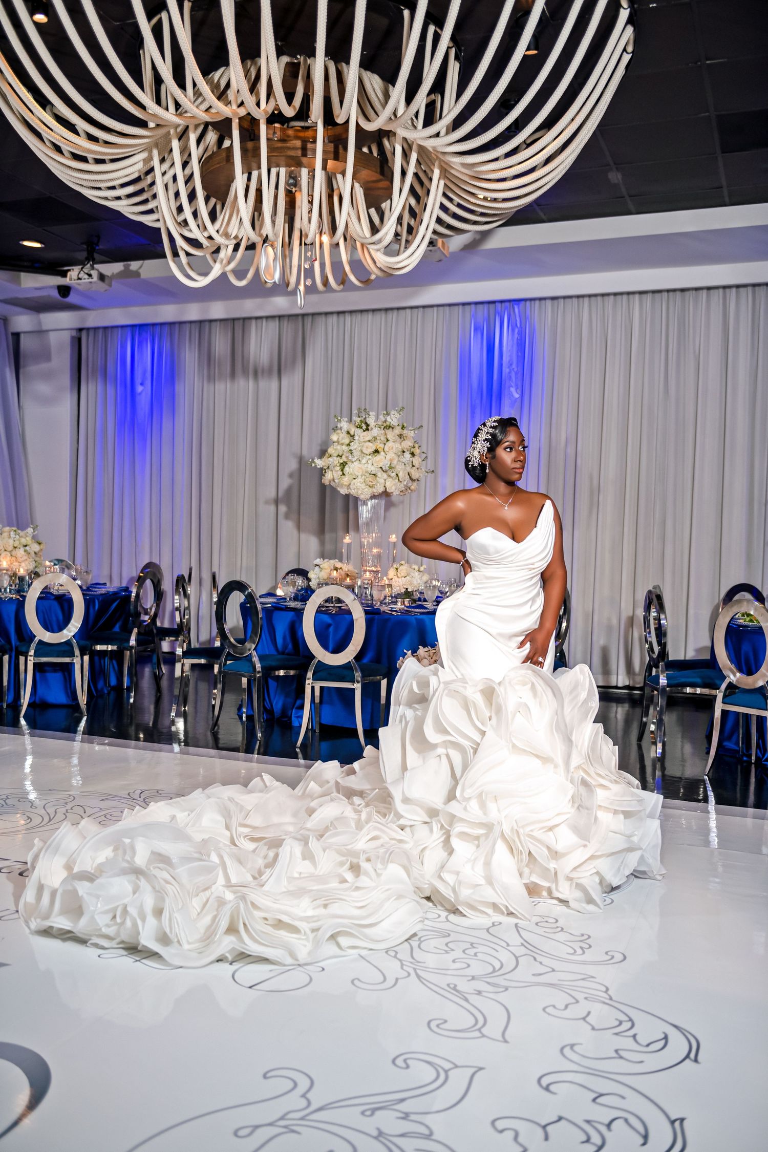 Stunning white mermaid wedding gown displayed in luxurious ballroom with modern chandelier and blue accents.