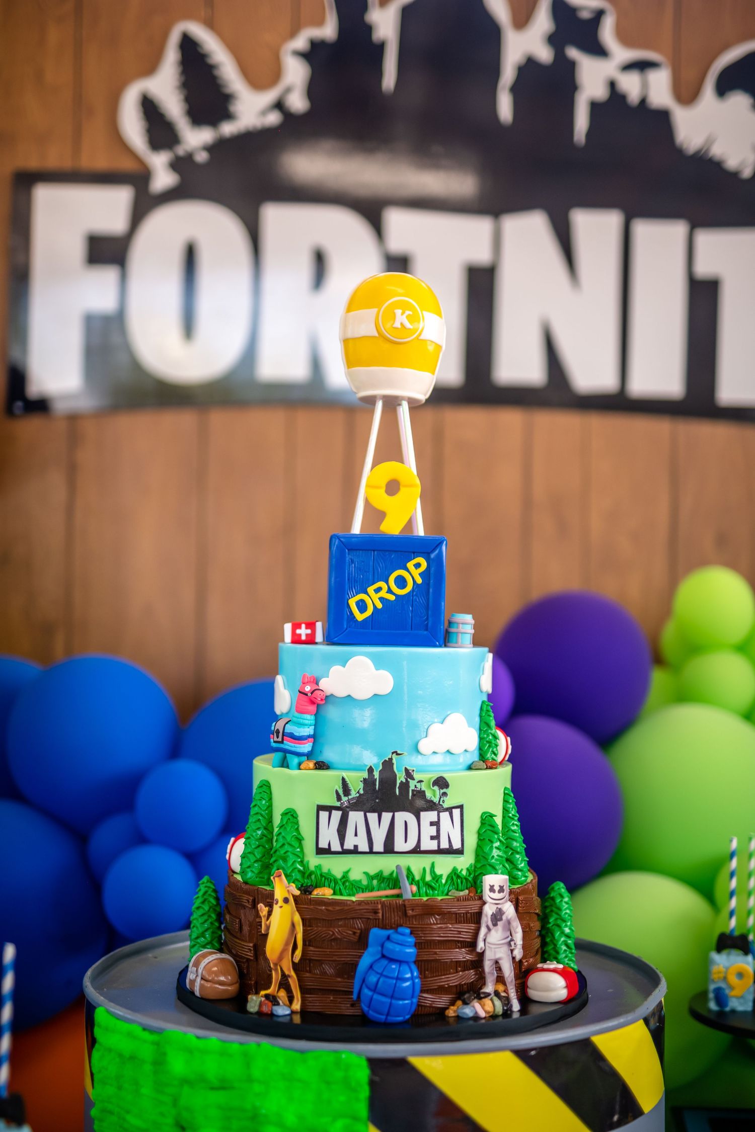 Fortnite themed birthday cake with gaming decorations and colorful balloon backdrop at a party celebration.