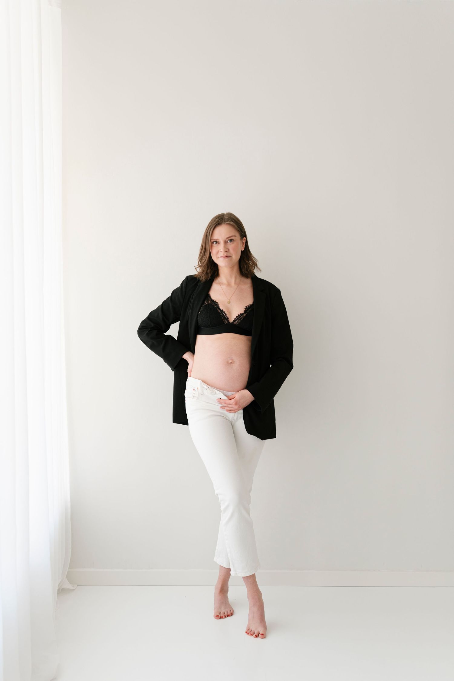 Maternity portrait with woman wearing black cardigan and white skirt in bright studio.