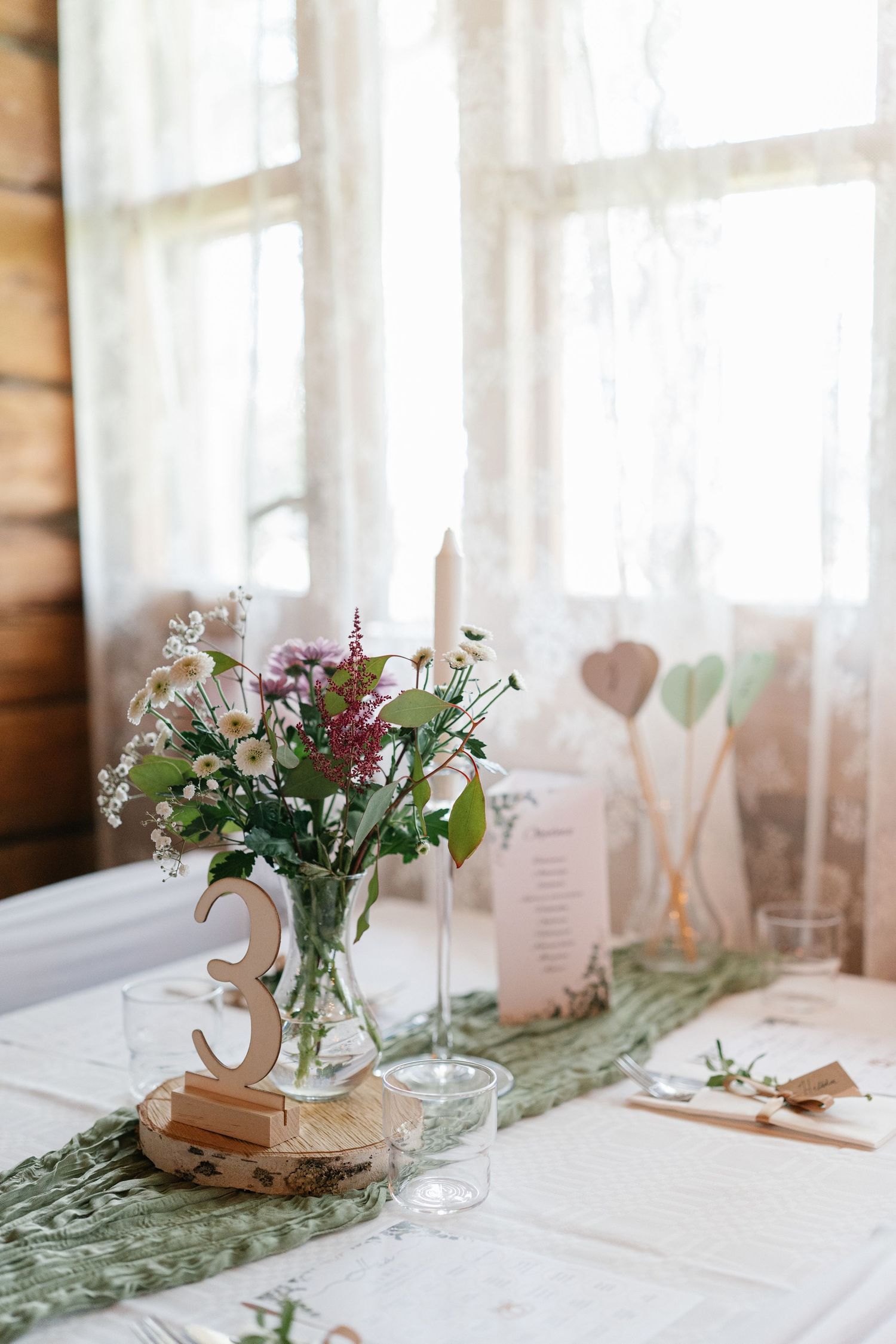 Wedding table centerpiece featuring wildflowers in glass vase with wooden table number.