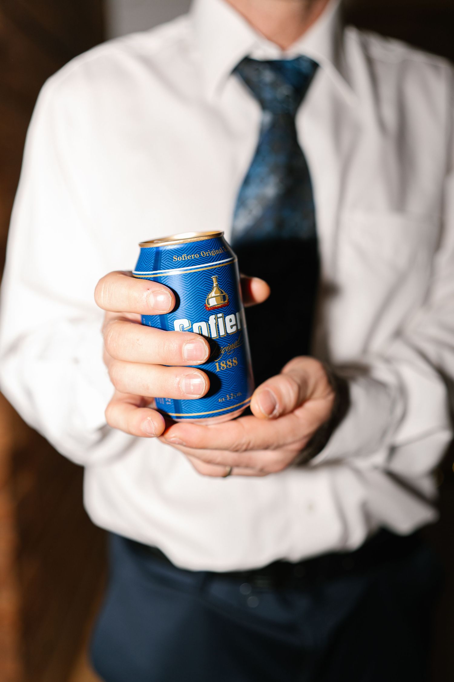 Person in formal attire holding a blue Brite beer can against dark background.