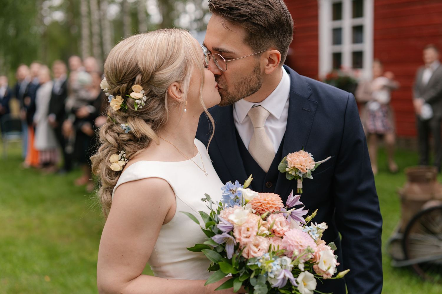 Wedding couple shares intimate moments against red building backdrop with peach floral bouquet.