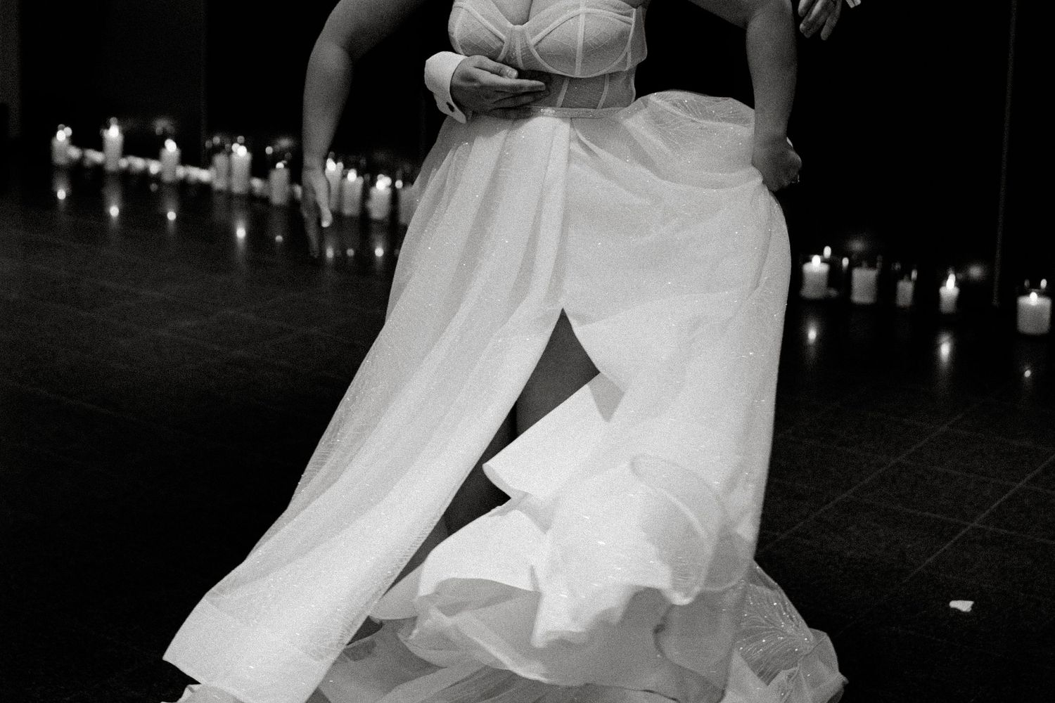 A flowing white wedding dress swirls dramatically during a dance on a dark reception floor.