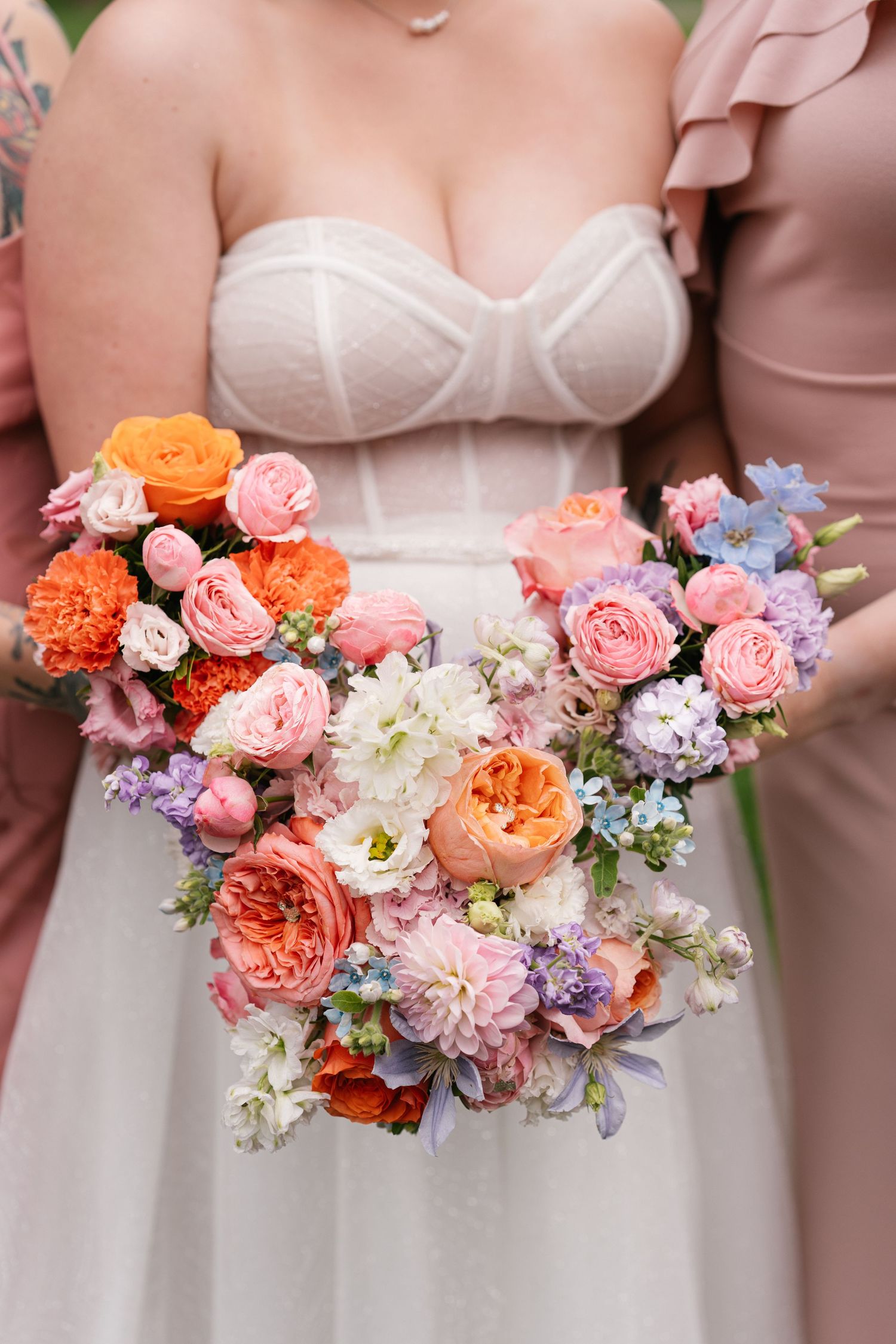 Bridesmaids hold vibrant coral and pink floral bouquets against blush dresses.