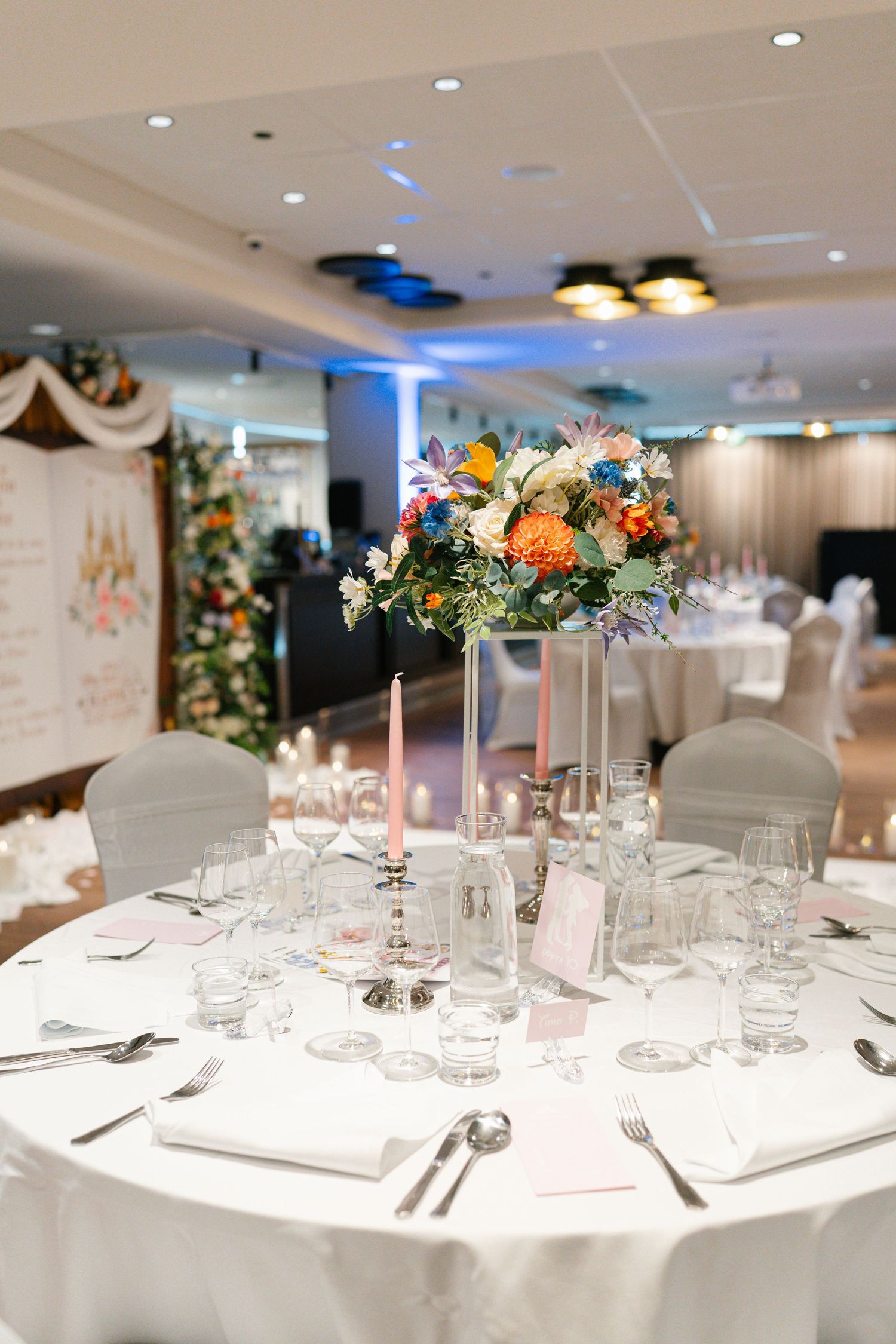 Elegant wedding reception tables set with white linens, glassware and floral centerpieces in a bright banquet room.