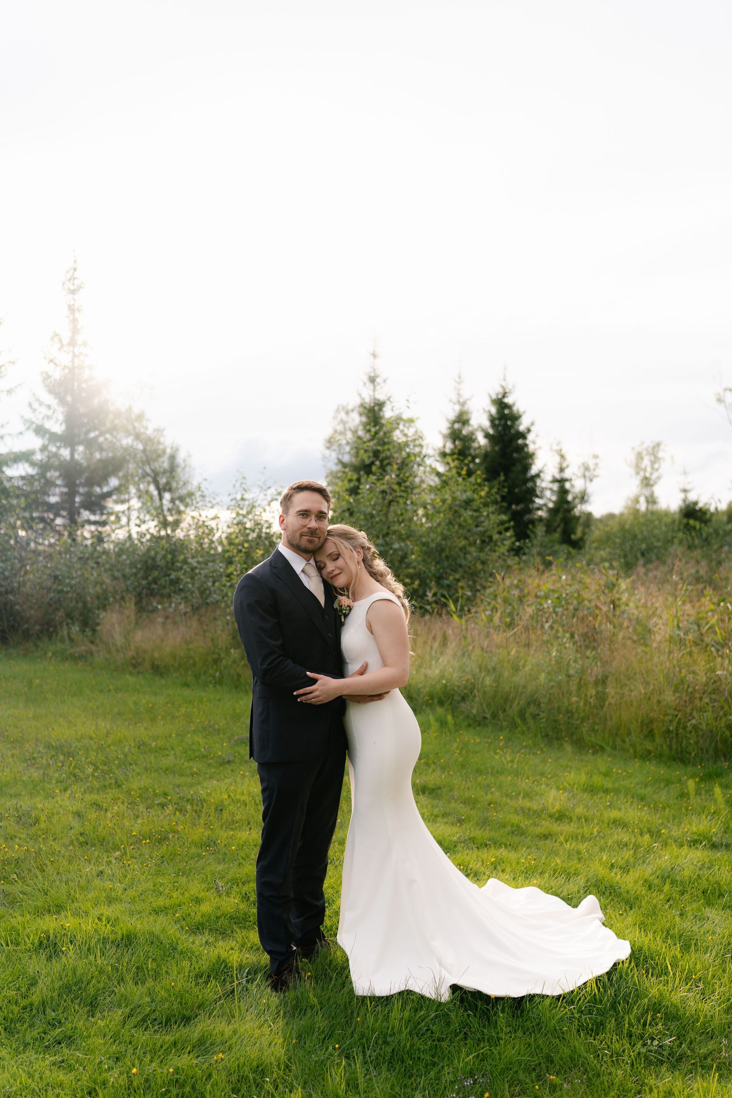 A bride in a flowing white dress and groom share intimate moments in a sunlit meadow.