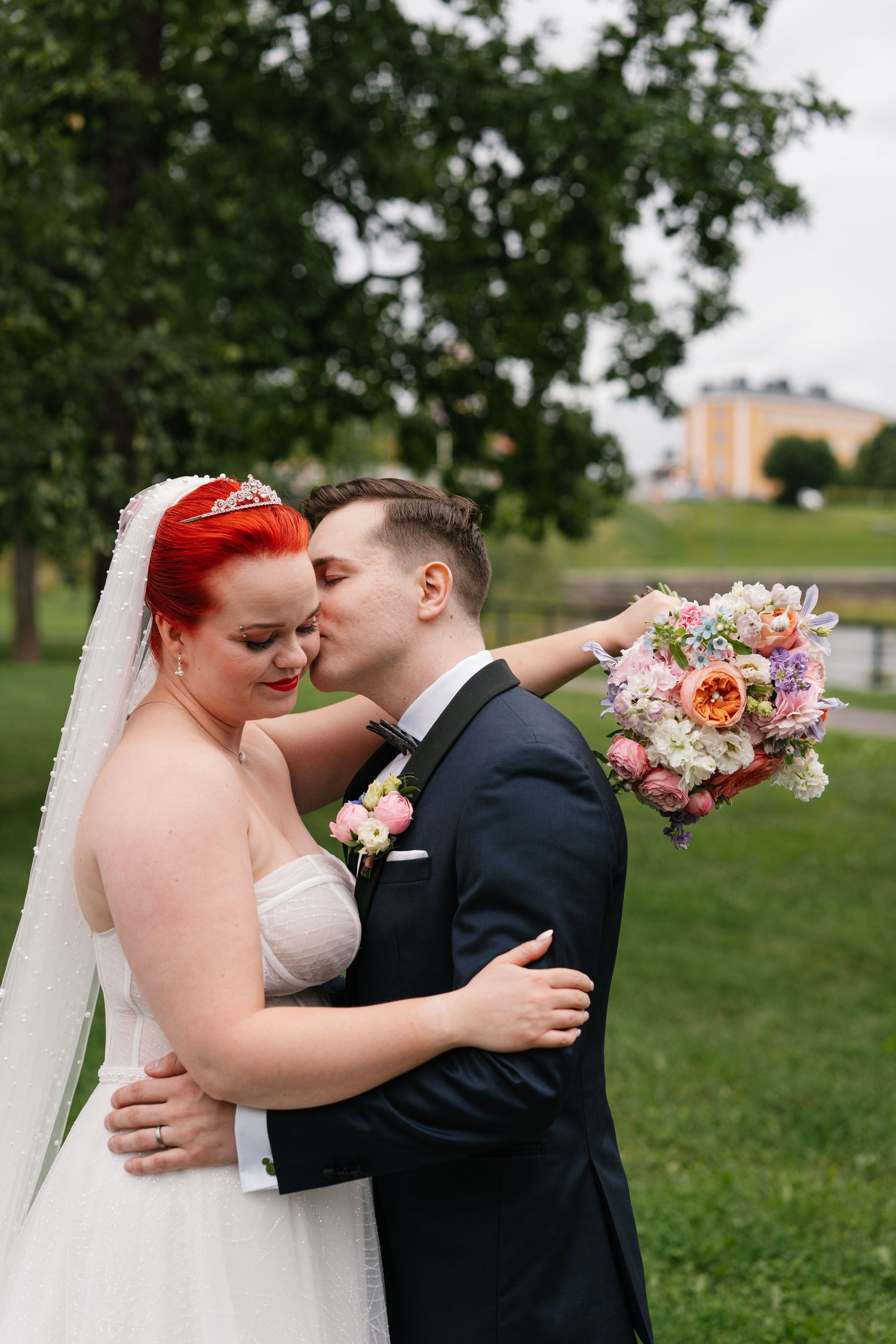 Romantic wedding couple embracing outdoors with colorful bouquet.