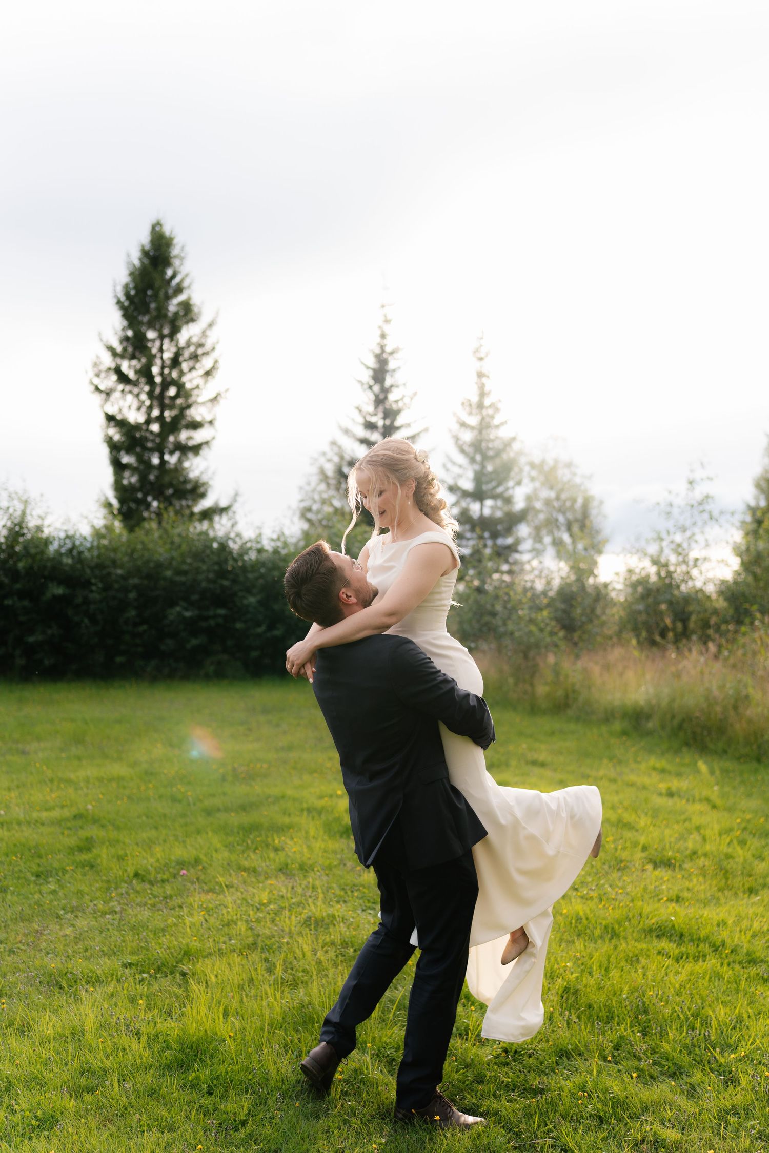 Romantic outdoor wedding moment in a grassy field with evergreen trees.