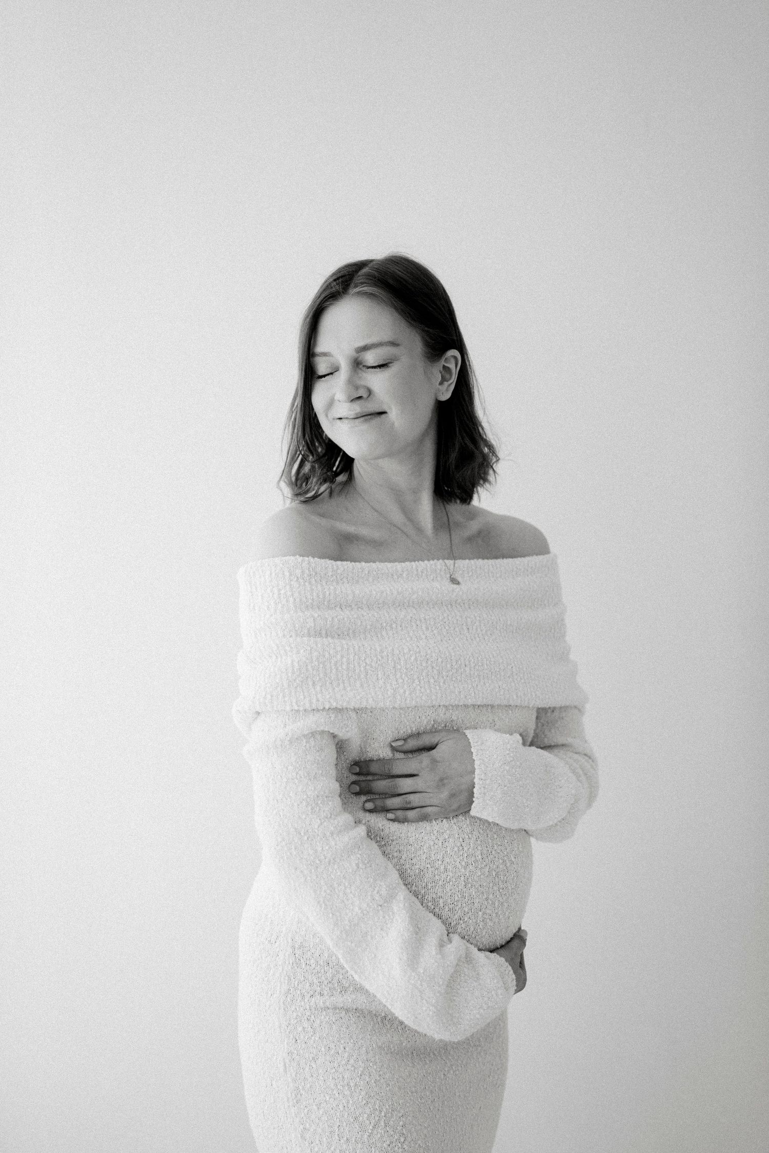 Artistic maternity photos showing woman in white off-shoulder dress against neutral background.