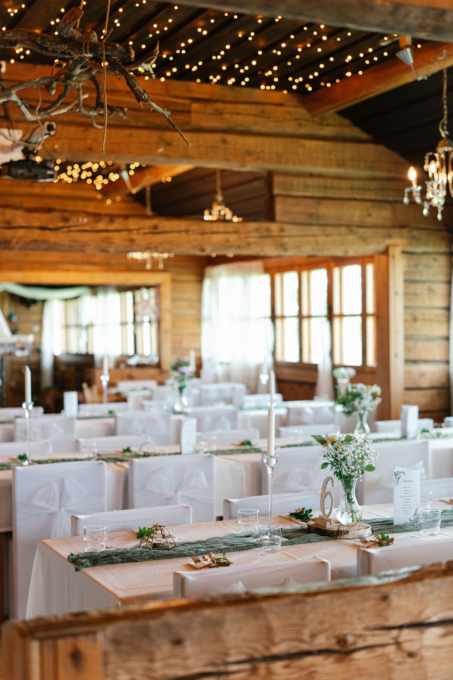 Rustic barn wedding reception setup with twinkling lights and white linens.